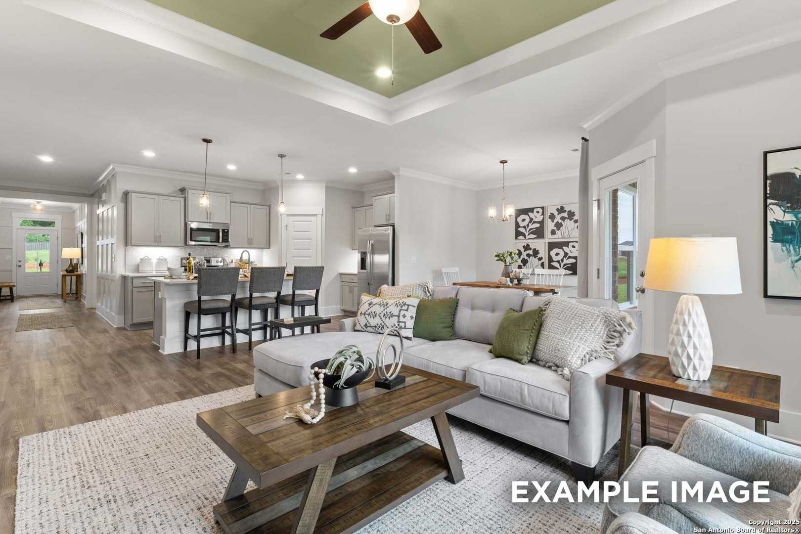 Open-concept living room and kitchen with white cabinets, gray sectional sofa, and ceiling fan in The Daphne H, Hannah Heights, Seguin, Texas