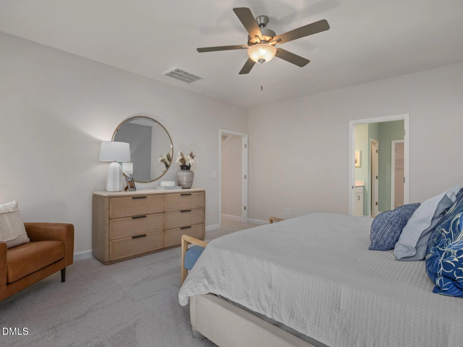 Serene master bedroom with king bed, blue pillows, wooden dresser, round mirror, ceiling fan in Davidson Homes The Hickory II D, Wake Forest, NC