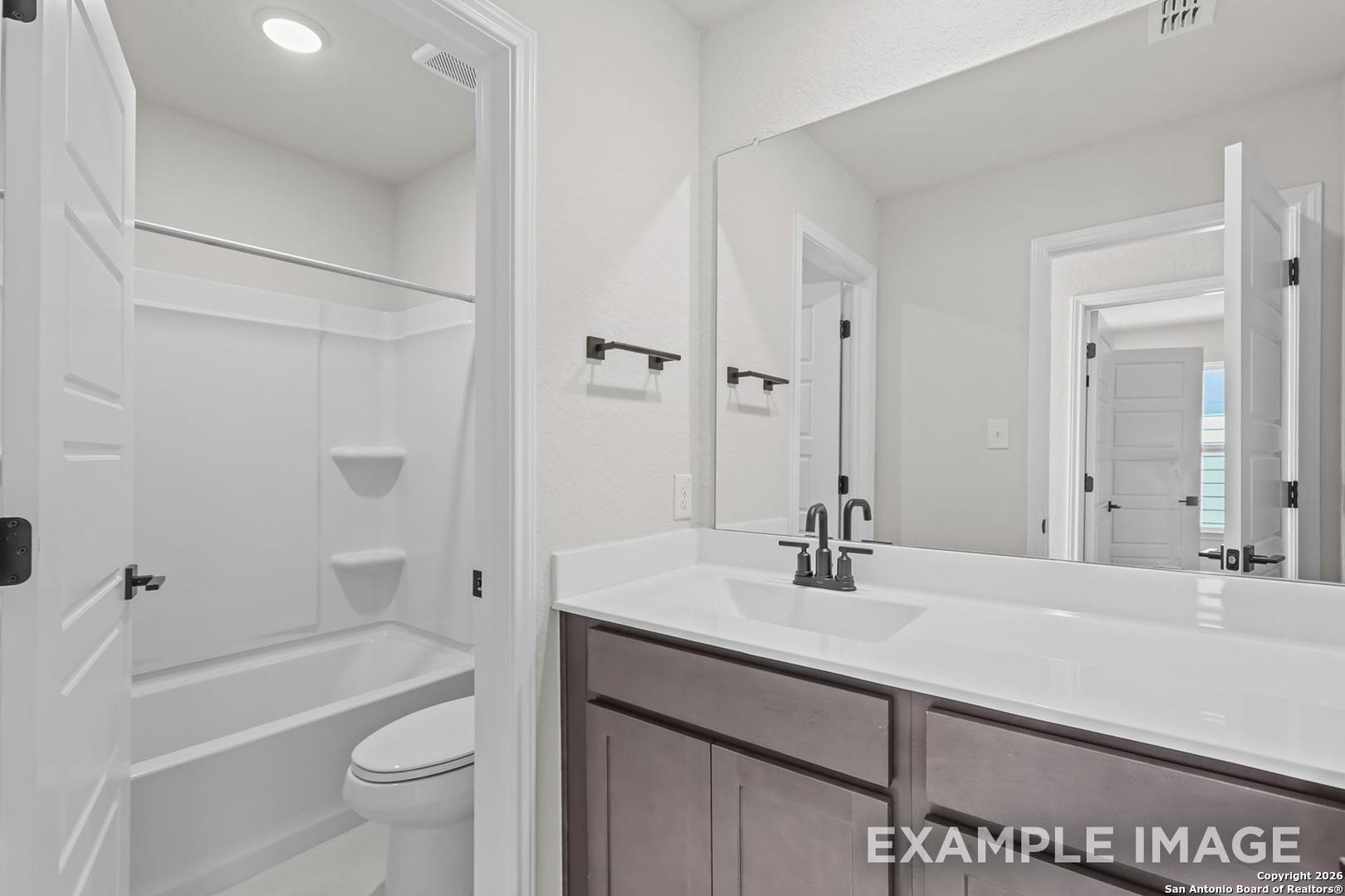 Contemporary secondary bathroom with tub-shower combo, brown vanity, and large mirror in Davidson Homes The Trinity B, San Antonio