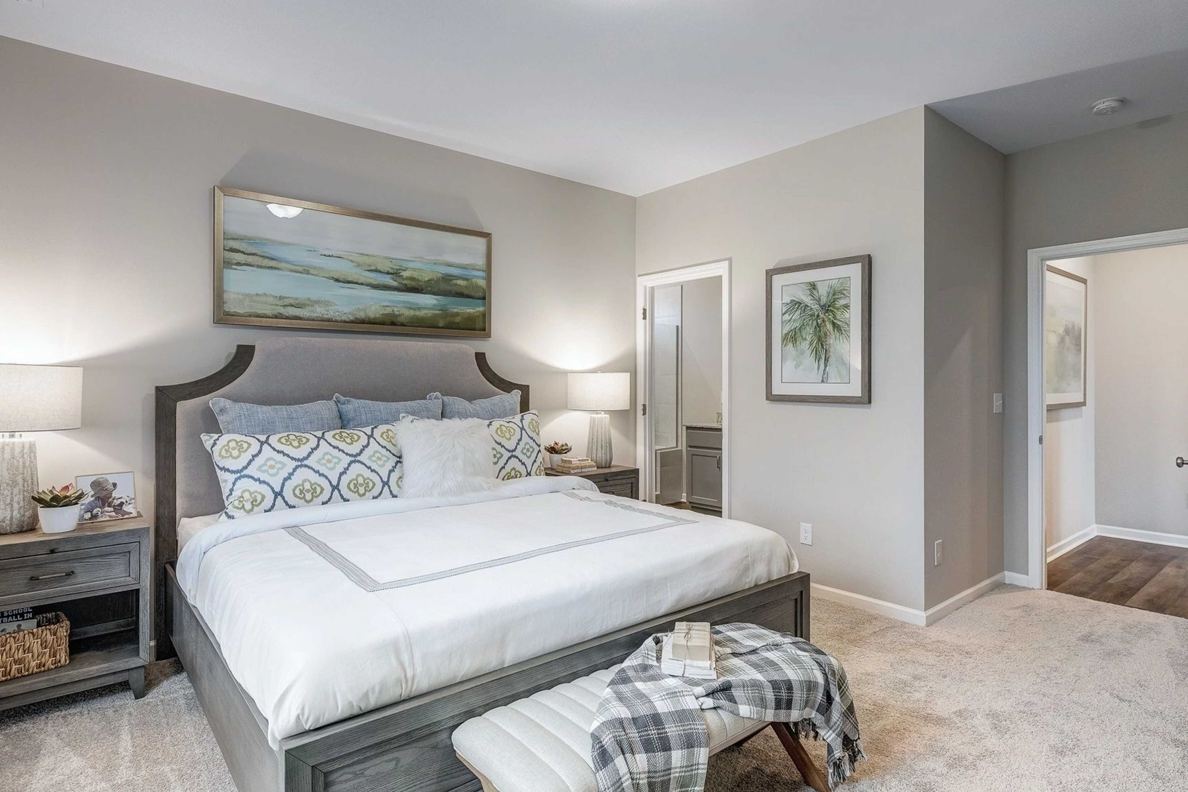 Coastal-inspired primary bedroom at Carroll Green in Harvest Alabama with king bed, gray headboard, neutral tones, and en-suite door