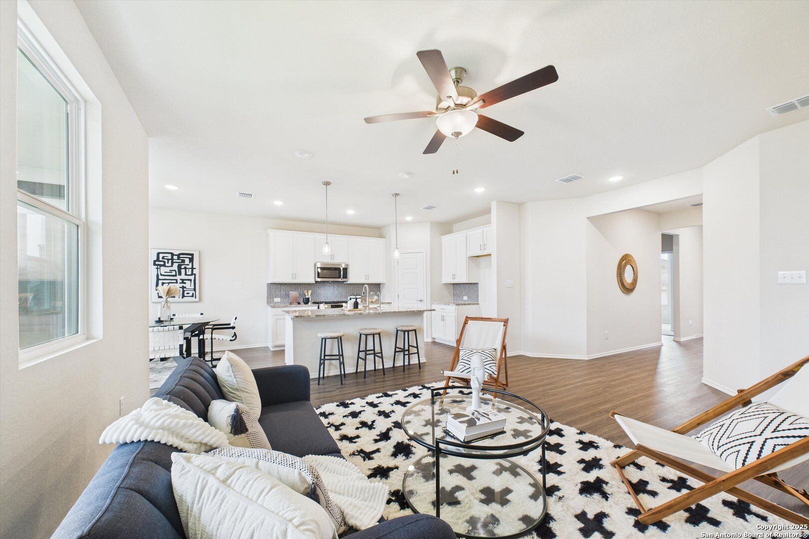 Open-concept living room with gray sectional sofa, patterned rug, and white kitchen bar in Davidson Homes Asheville K, Bricewood San Antonio
