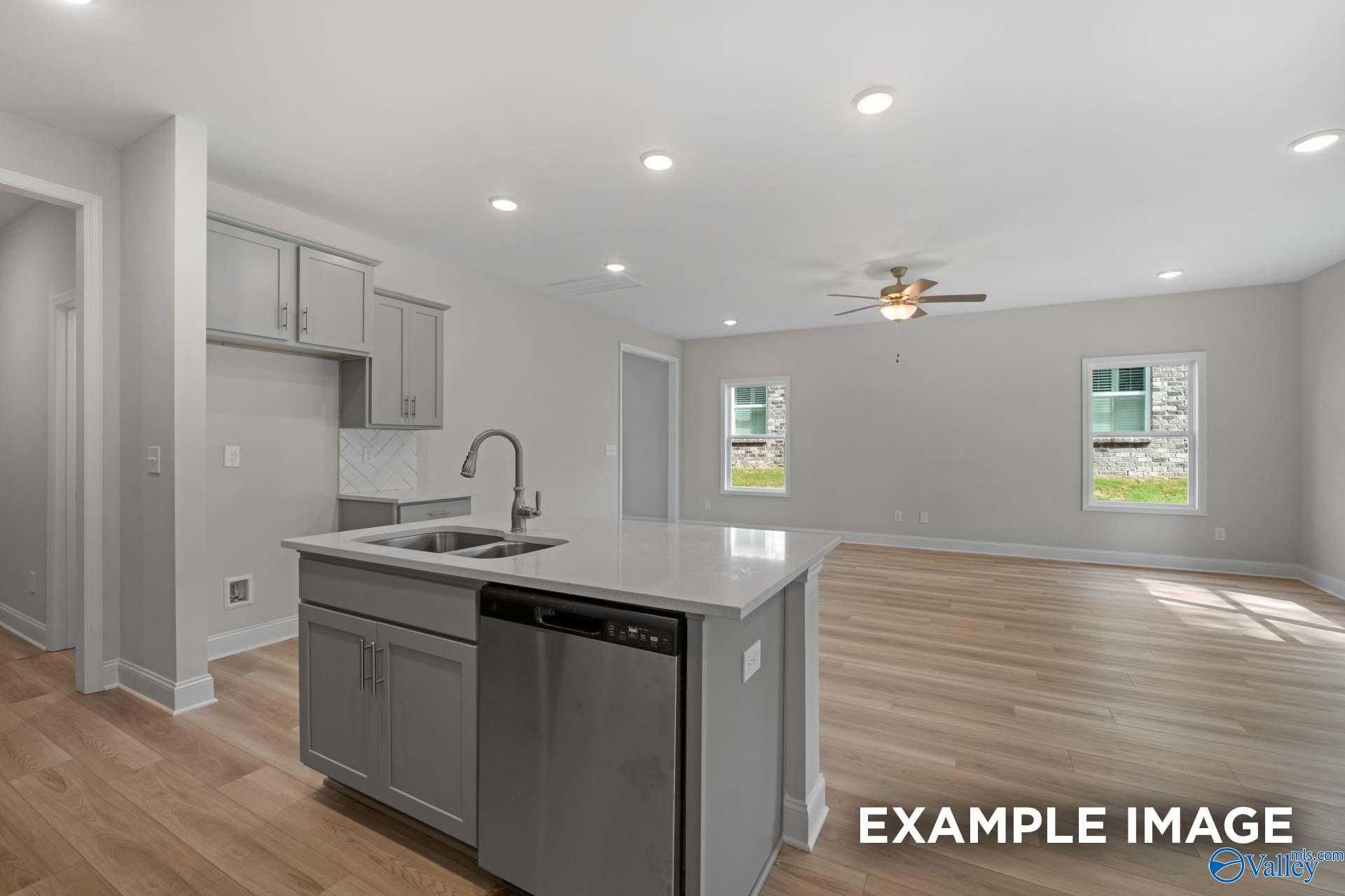 Modern open-concept kitchen with gray cabinets, quartz island sink, stainless dishwasher, and hardwood floors in Davidson Homes The Camden, Huntsville AL
