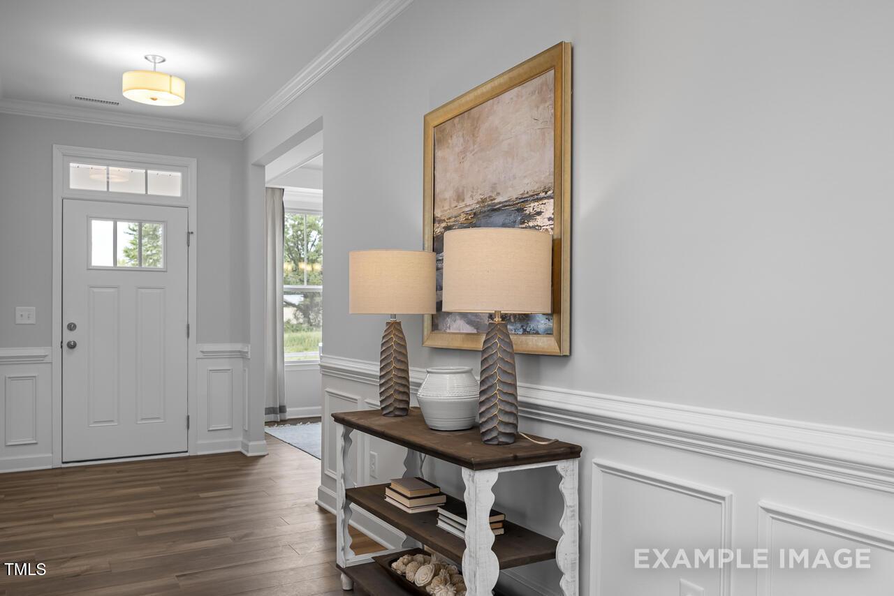 Welcoming entryway with white front door, hardwood floors, console table, lamps, and abstract art in Davidson Homes Magnolia B, Angier, NC