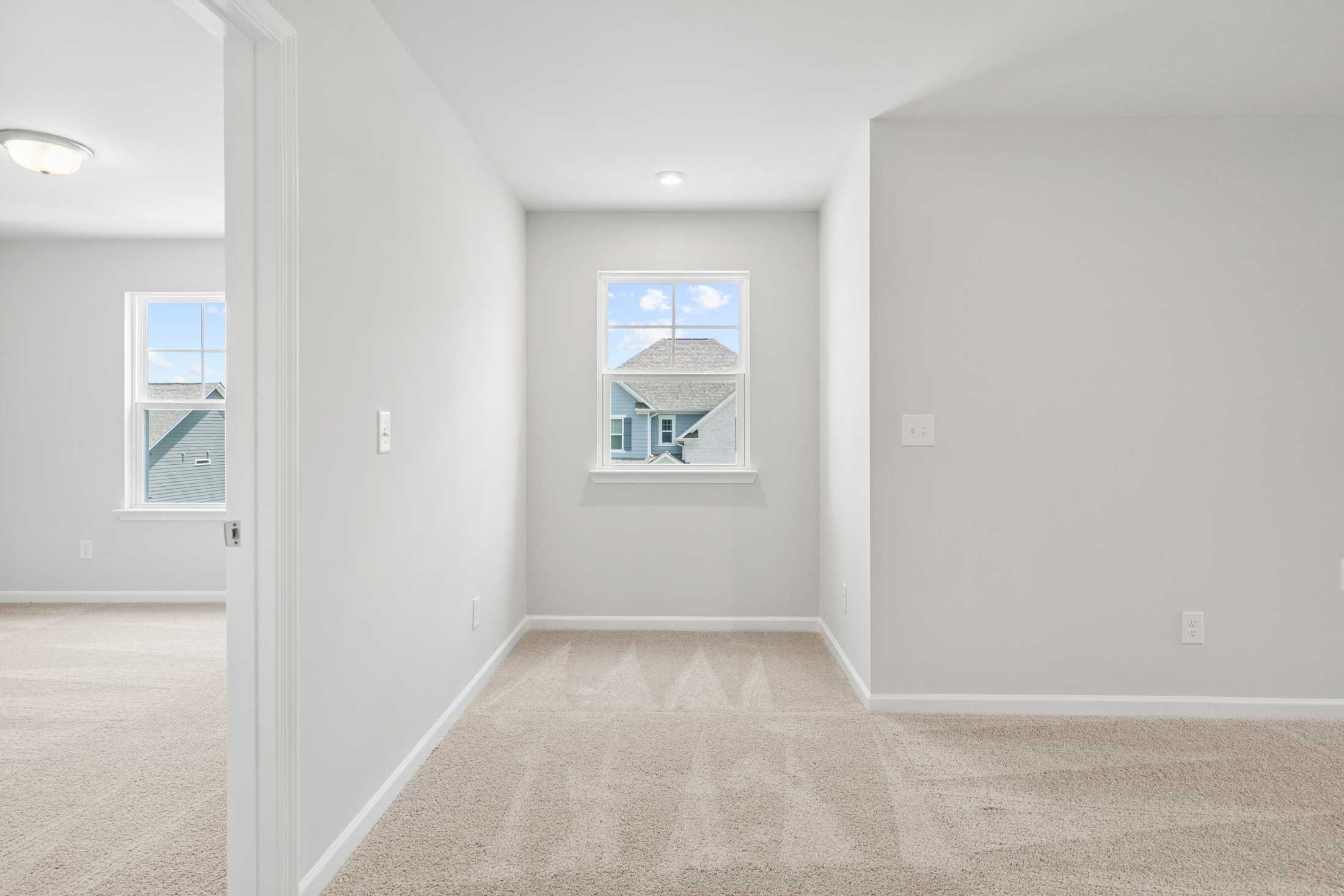 Spacious upstairs hallway in The Ash B featuring light gray walls, beige carpet, and window view of neighborhood homes