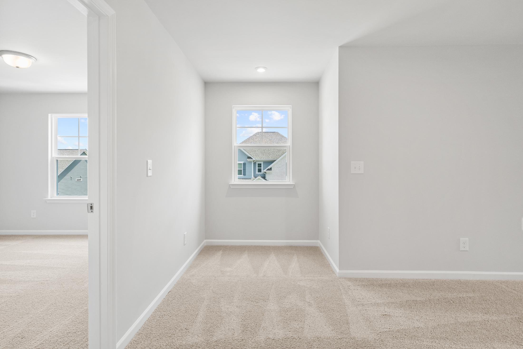 Spacious upstairs hallway in The Ash B featuring light gray walls, beige carpet, and window view of neighborhood homes
