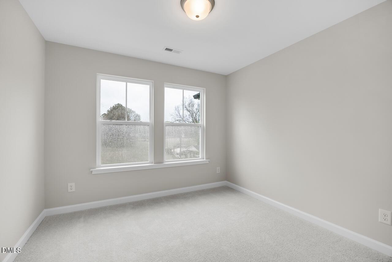 Bright secondary bedroom featuring light gray walls, plush carpet, and dual windows with tree views in Davidson Homes The Avery, Knightdale, NC