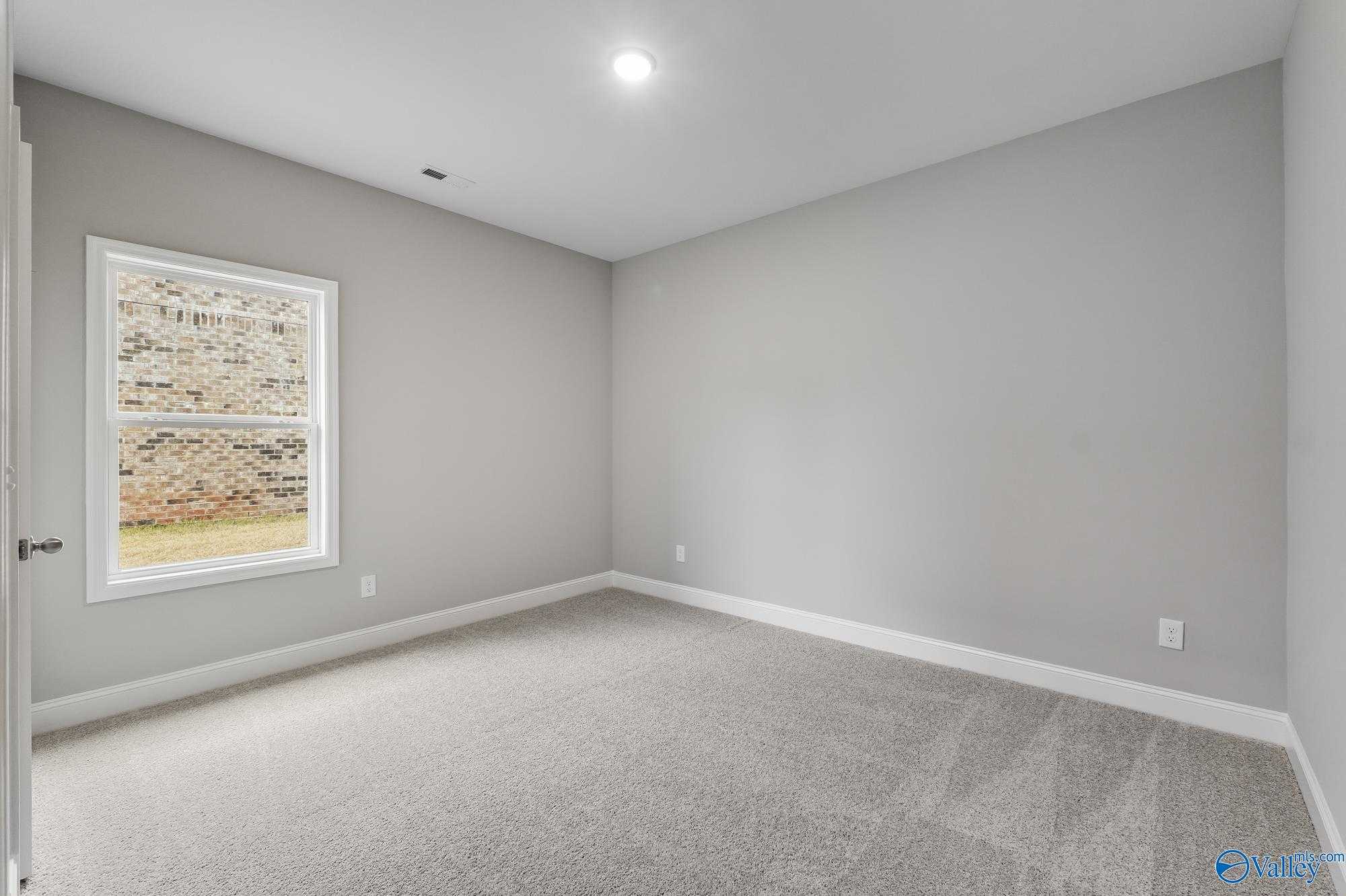Spacious empty bedroom with gray walls, neutral carpet, and large window in 4-bedroom The Daphne D home, Athens, Alabama