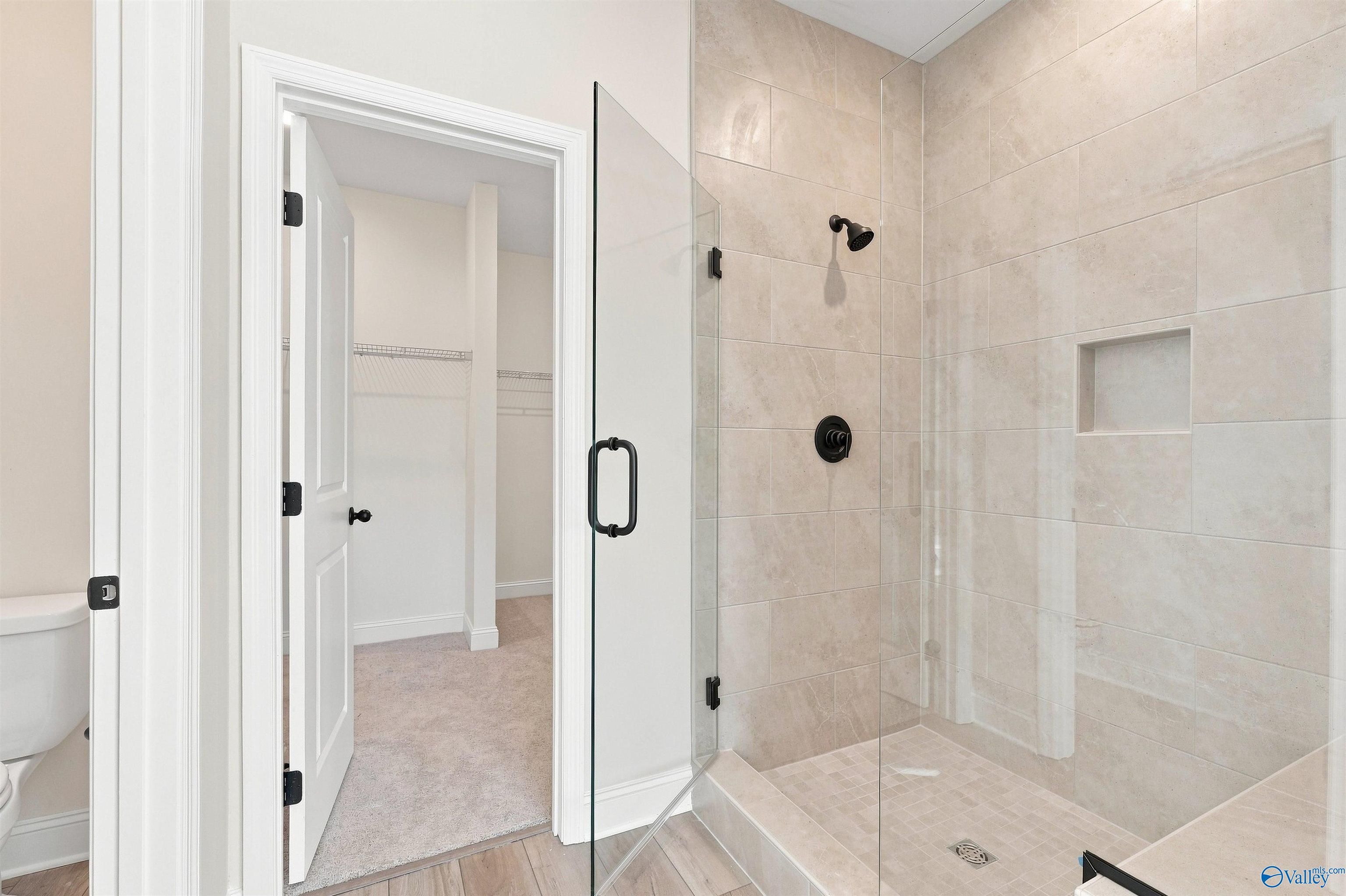 Elegant master bathroom with glass-enclosed tile shower, matte black fixtures, and walk-in closet in Davidson Homes The Everett B, Toney, Alabama