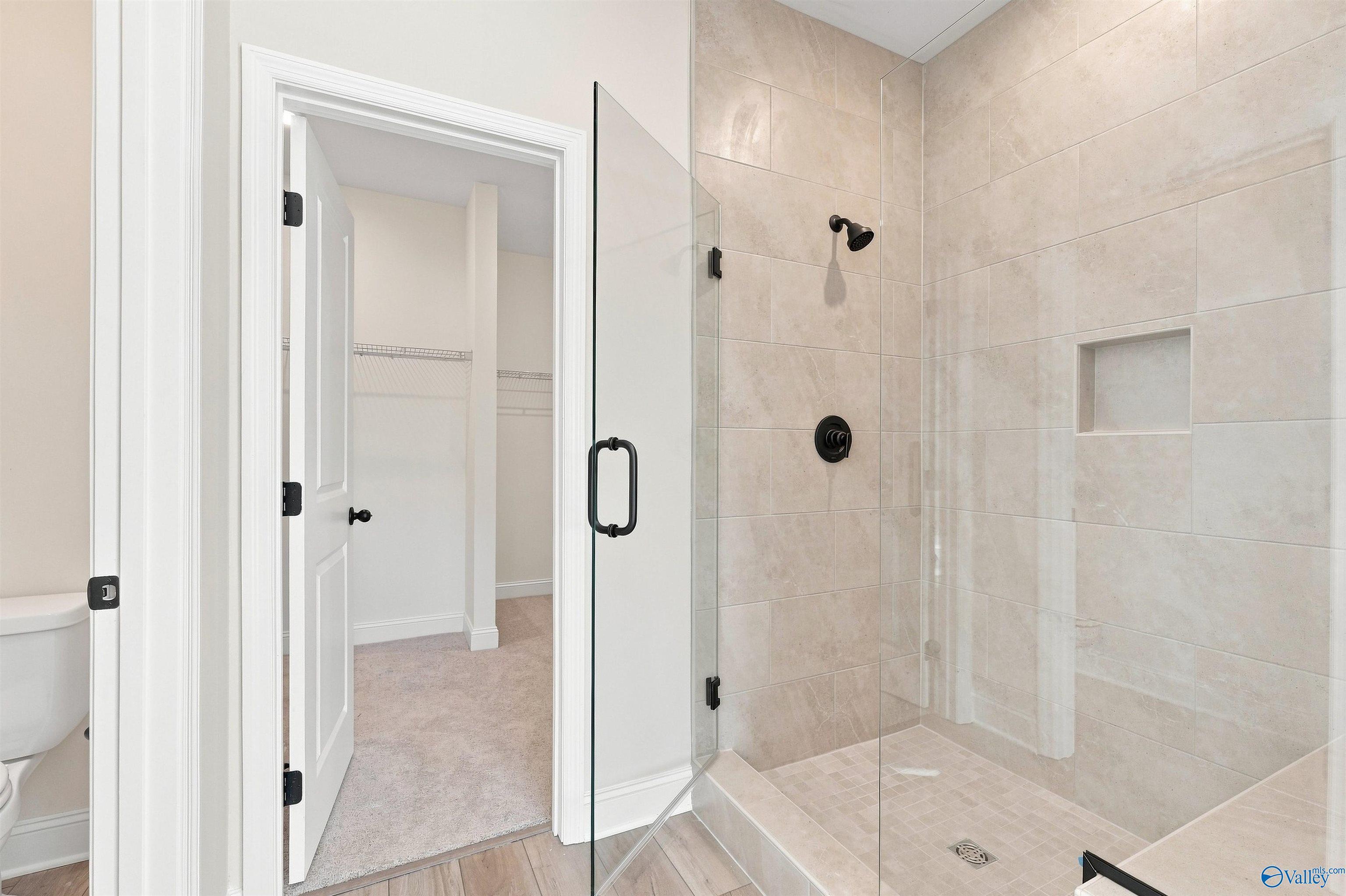 Elegant master bathroom with glass-enclosed tile shower, matte black fixtures, and walk-in closet in Davidson Homes The Everett B, Toney, Alabama