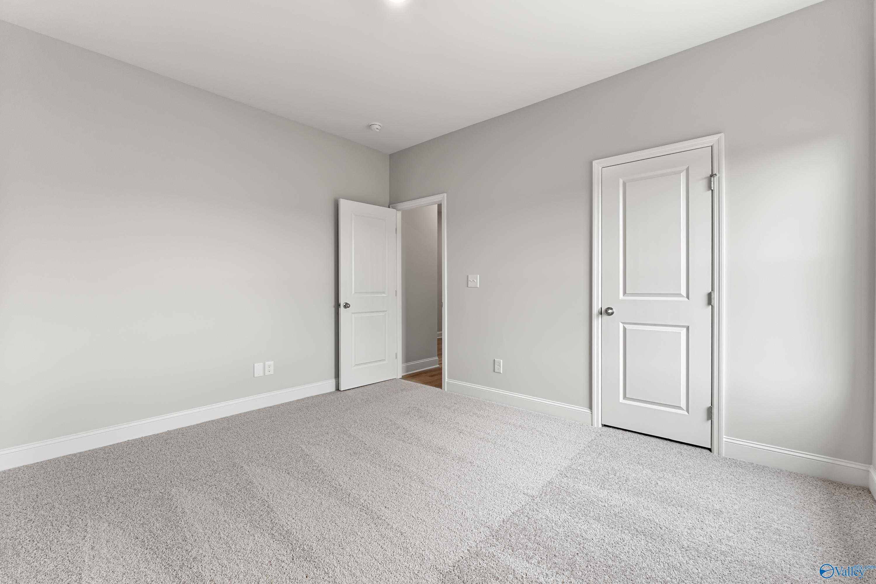 Empty bedroom with light gray walls, white doors, and plush carpet in The Daphne C 4-bedroom home, Davidson Homes, Athens, Alabama