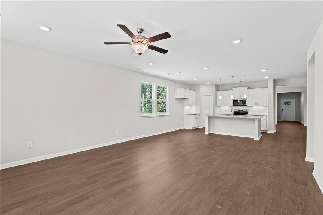 Open-concept great room with kitchen island, hardwood floors, large windows, and ceiling fan in The Orion 4-bedroom home, Cusseta, Alabama