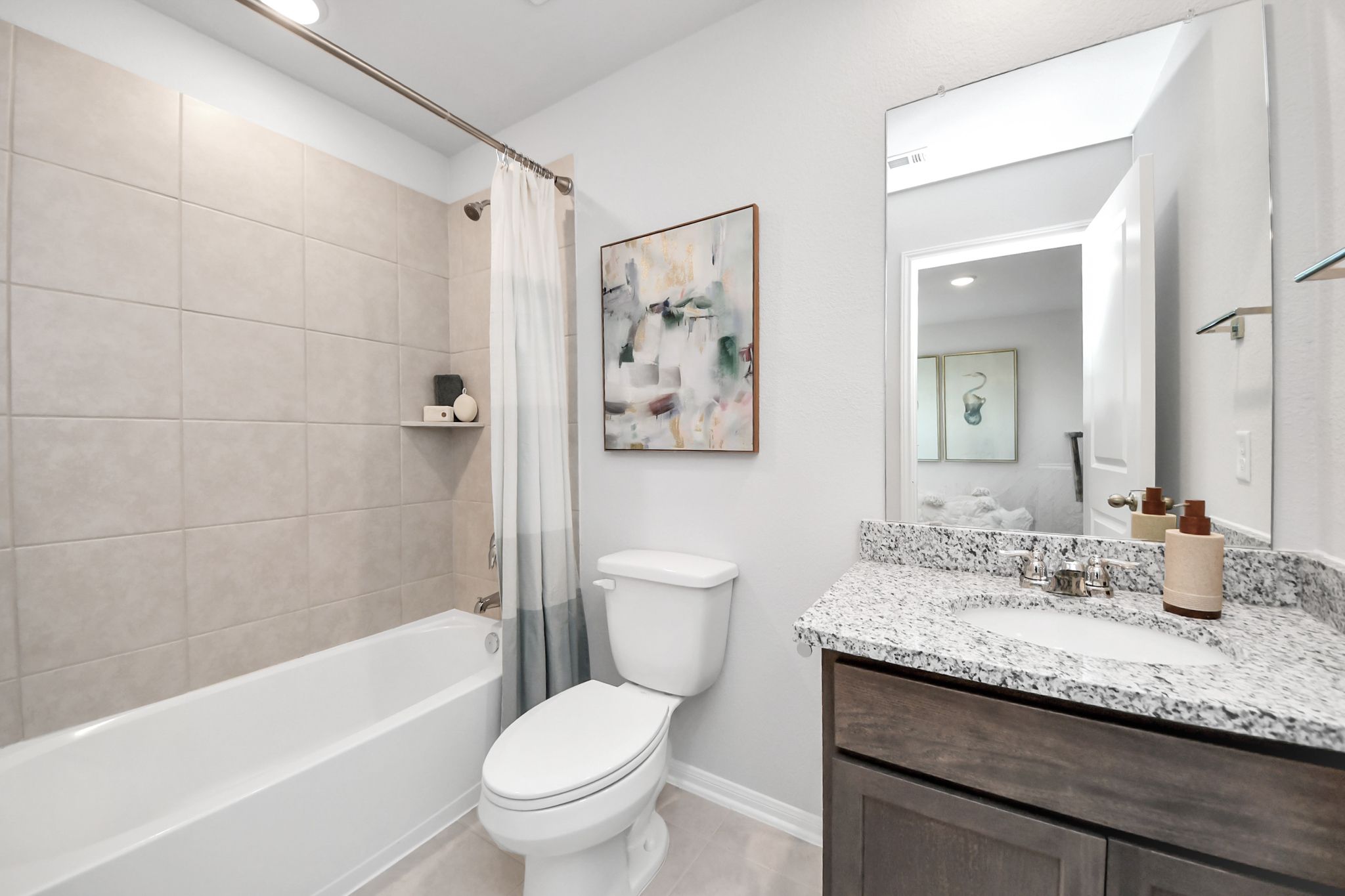 Modern bathroom in Sunterra community by Davidson Homes in Katy, Texas, featuring granite vanity and tiled tub-shower.