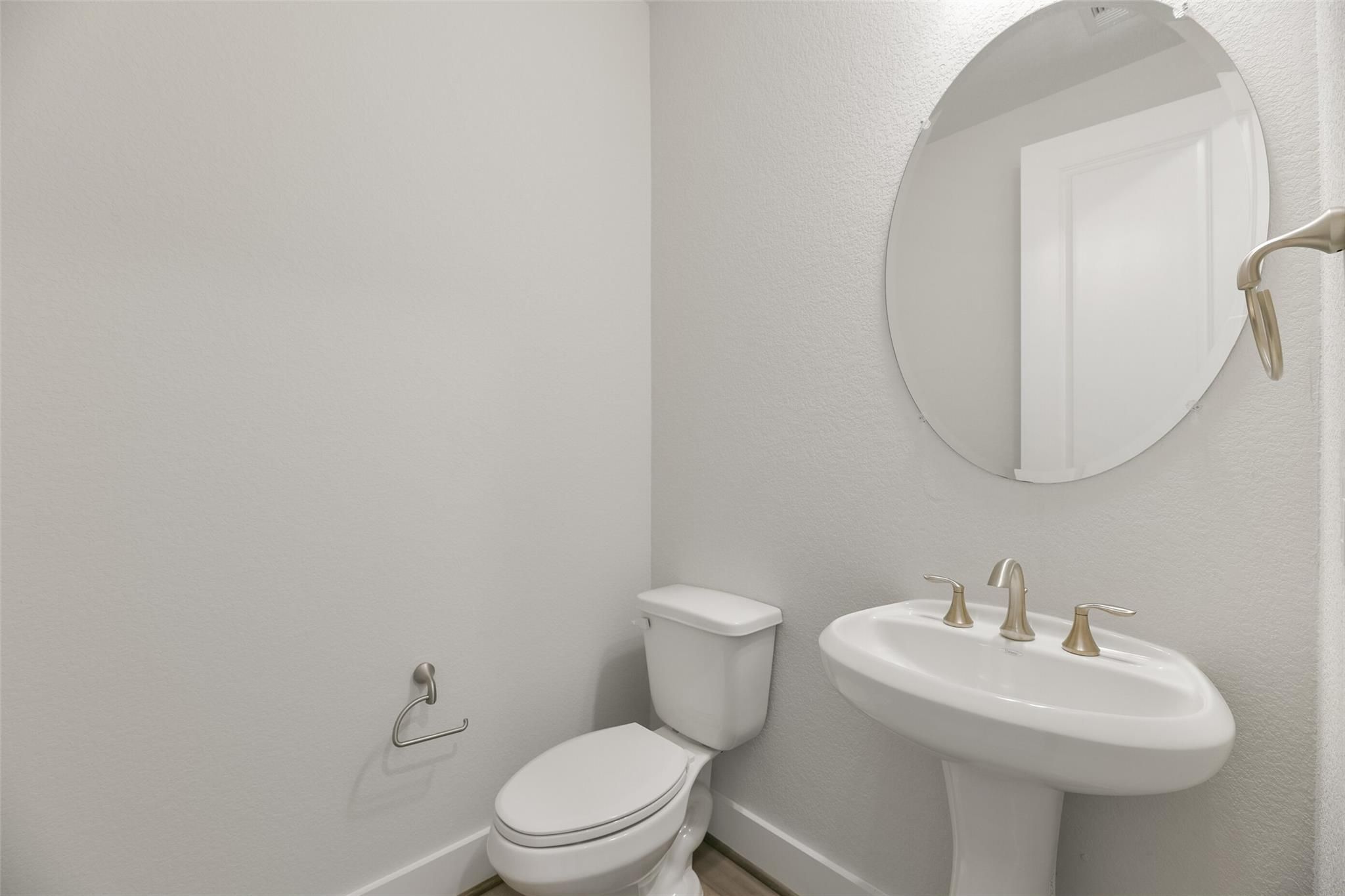 Elegant powder room with round mirror, pedestal sink, gold faucets, and toilet in Davidson Homes The Edward A, Texas City