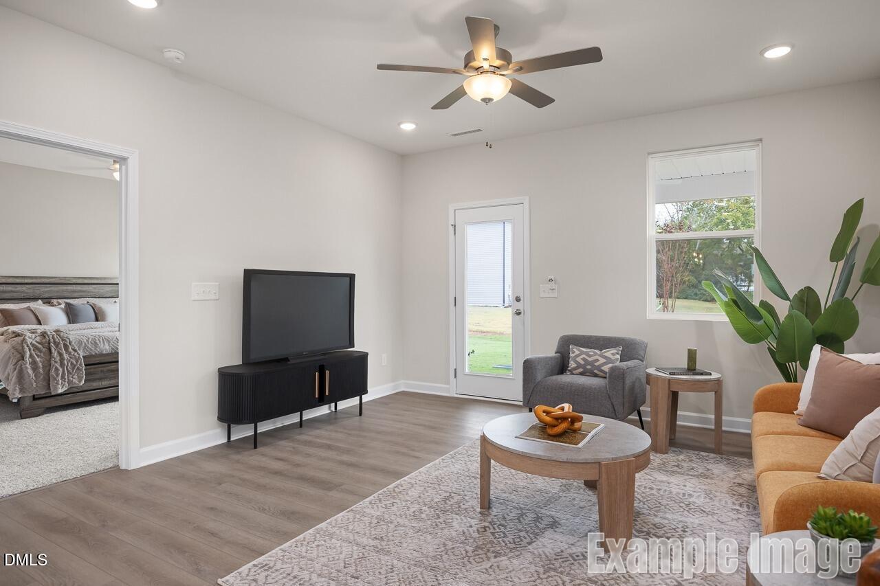 Cozy living room with orange sofa, TV console, ceiling fan, and backyard door in Davidson Homes The Carter C, Lillington, NC