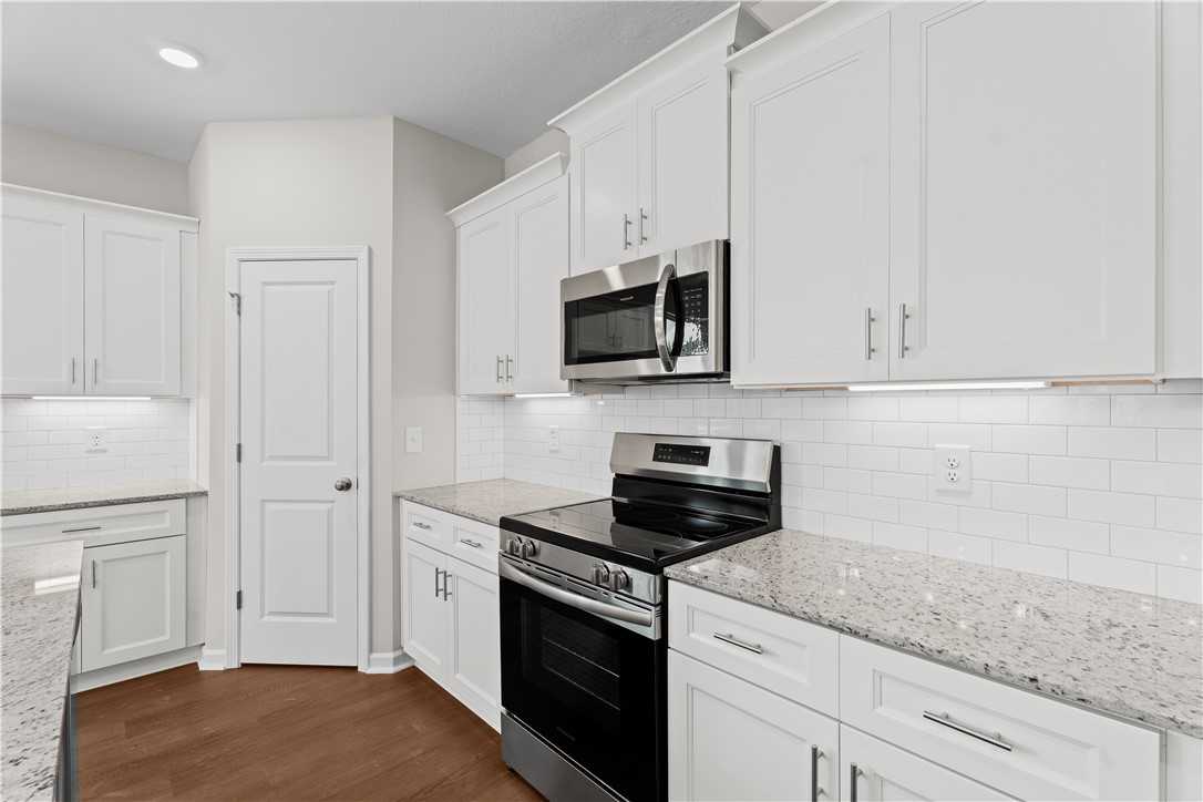 Modern kitchen with white shaker cabinets, speckled granite counters, stainless appliances in Evermore Homes Orion, Cusseta, Alabama