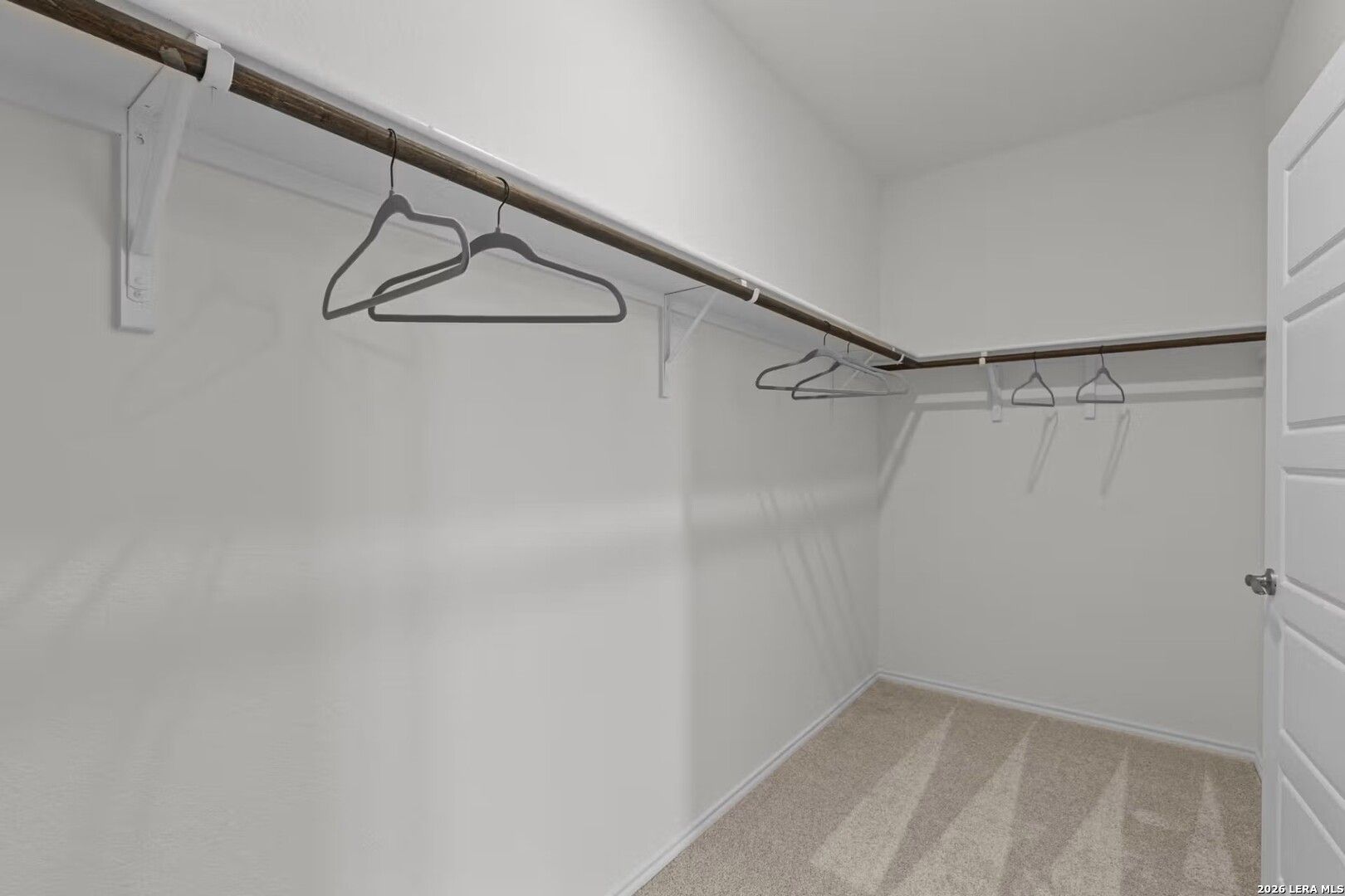 Spacious walk-in closet with wooden rods, gray hangers, and beige carpet in master suite of Davidson Homes The Daphne K in San Antonio