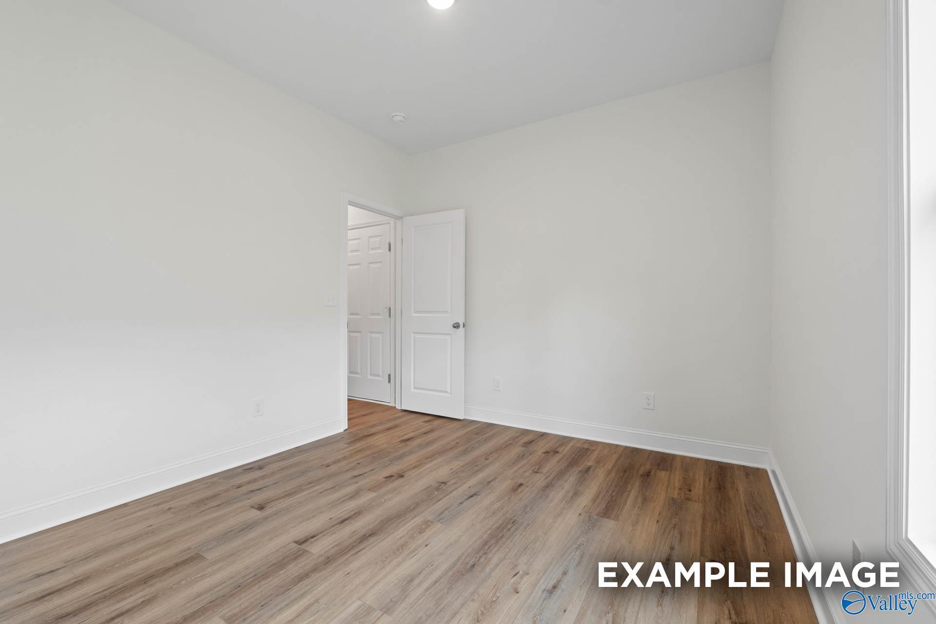 Bright empty bedroom with laminate wood floors and white walls in Evermore Homes Daphne E, Harvest AL