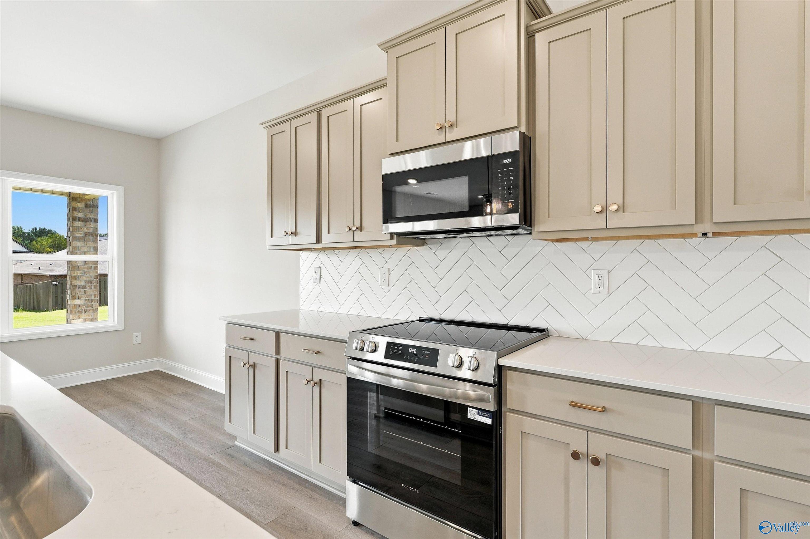 Modern kitchen with taupe shaker cabinets, herringbone tile backsplash, stainless appliances in Davidson Homes The Shelby A, Athens, AL