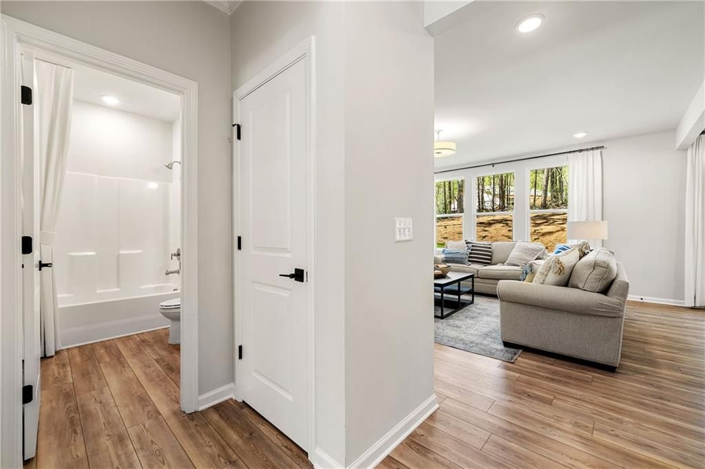 Cozy living room with beige sectional sofa, coffee table, and wooded views adjacent to guest bathroom in 5-bedroom Davidson Homes The Willow B, Dallas Georgia