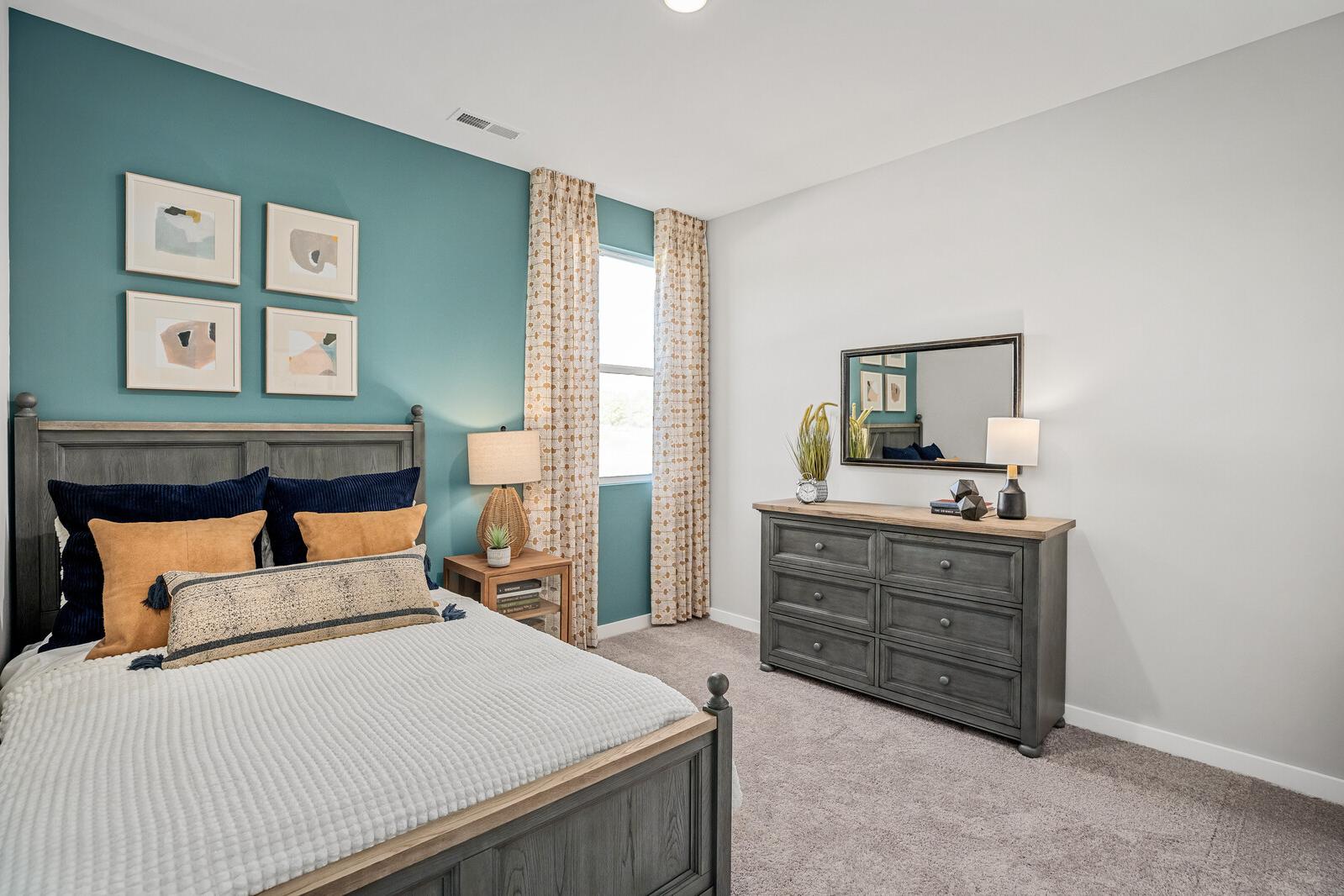 Spacious primary bedroom at Sage Farms in White House TN by Davidson Homes with teal accent wall, wooden bed frame, dresser, and window seating