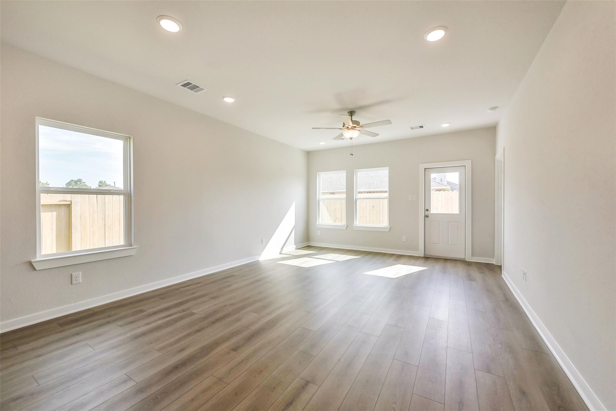 Spacious living room with hardwood floors, ceiling fan, large windows, and double doors in Davidson Homes The Comal G, Dayton Texas