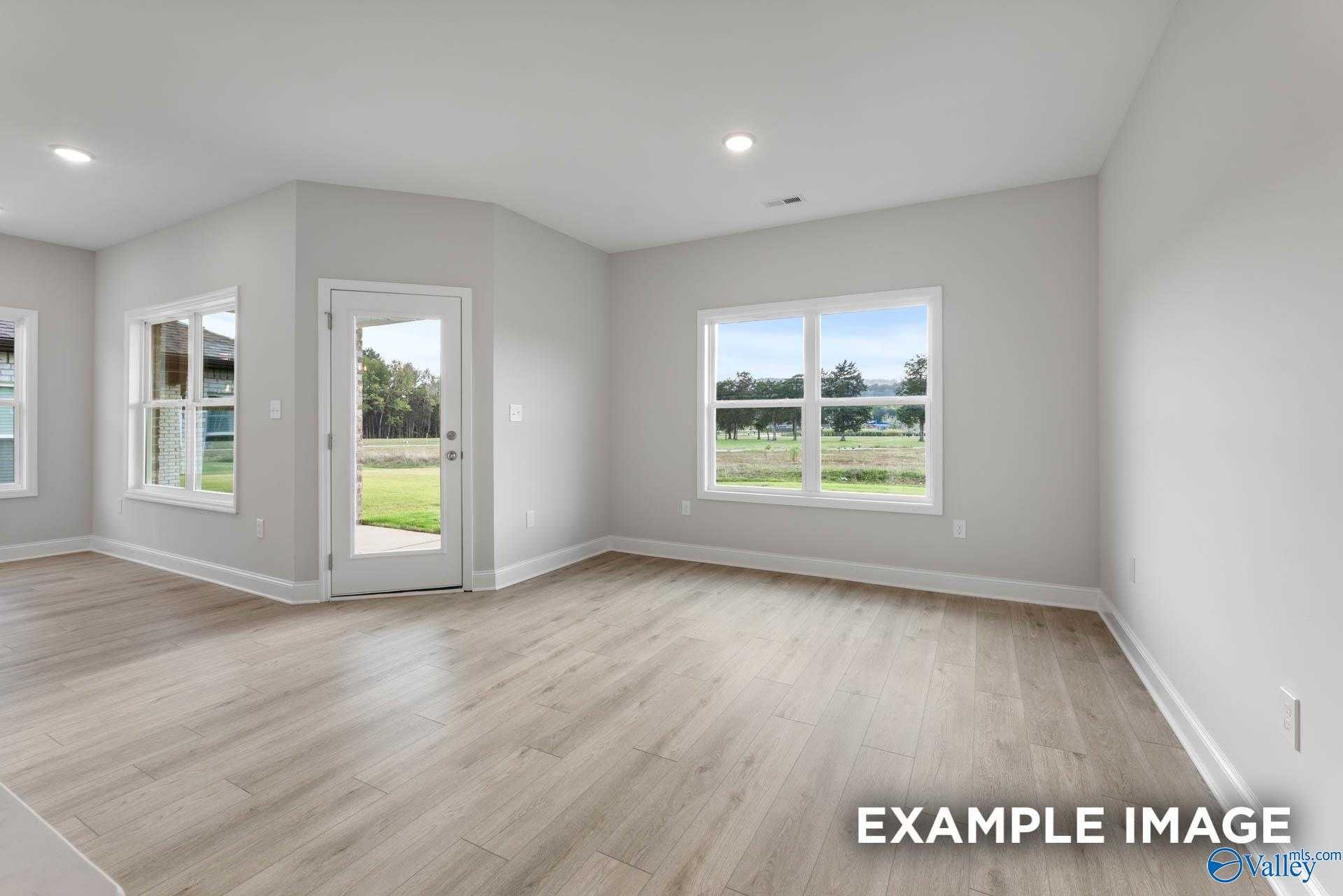 Bright living room with large windows overlooking lush backyard, gray walls, hardwood floors in Davidson Homes The Franklin C, Athens AL