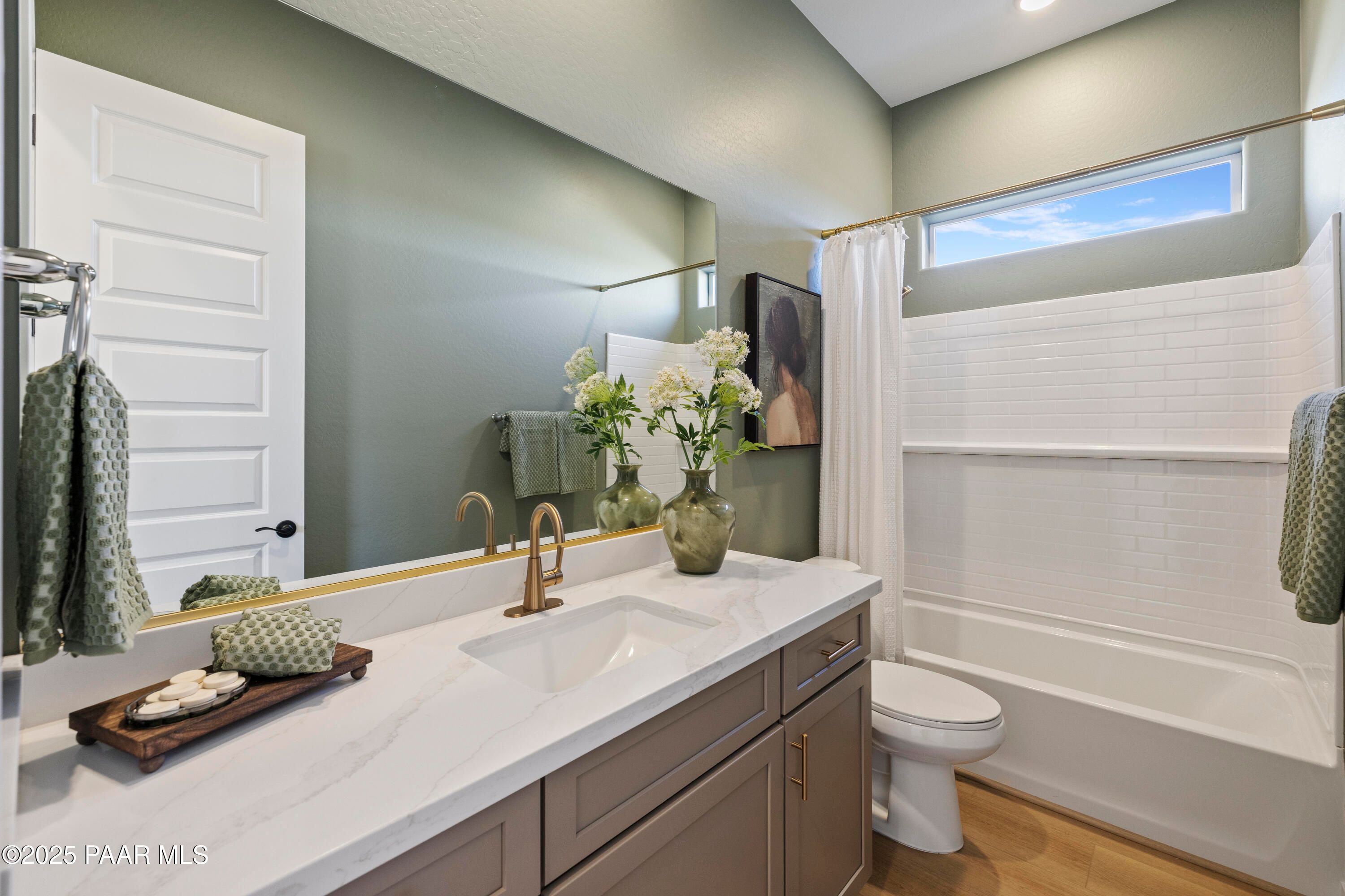 Elegant sage green bathroom with quartz vanity, gold fixtures, subway tile shower, and tub in Davidson Homes The Blaze D, Prescott, Arizona