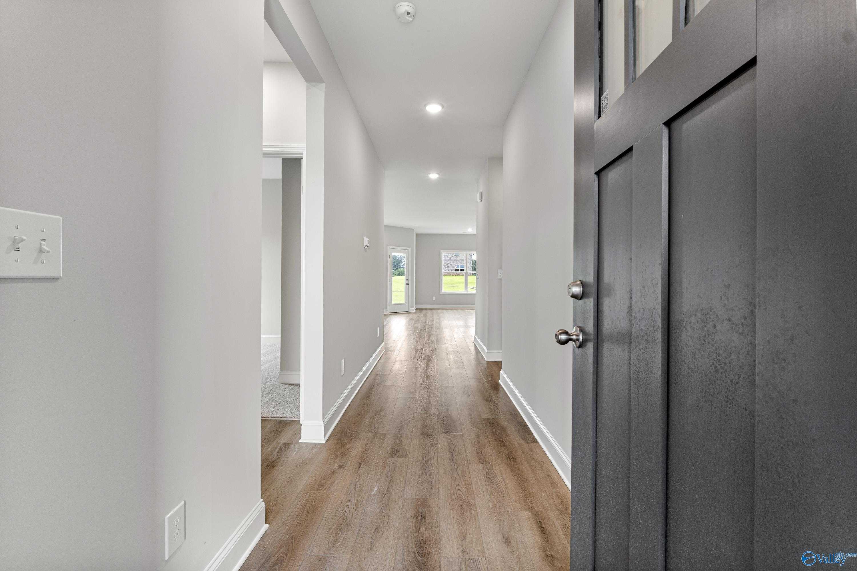 Spacious hallway with light oak flooring, white walls, and dark front door in The Franklin 3-bedroom home, Athens, Alabama