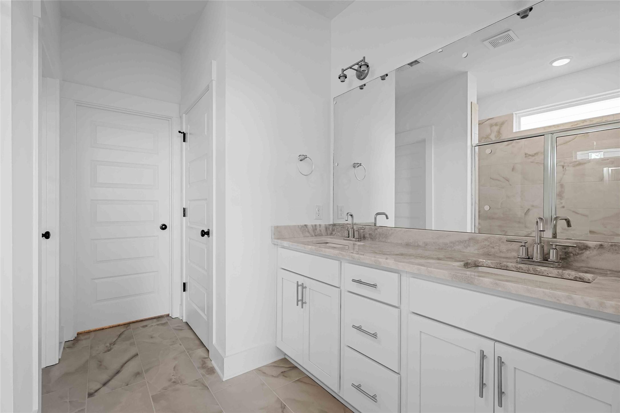 Modern bathroom with dual vanity, marble countertops, and tiled walk-in shower in The Ash O floor plan, Heartland, Texas.