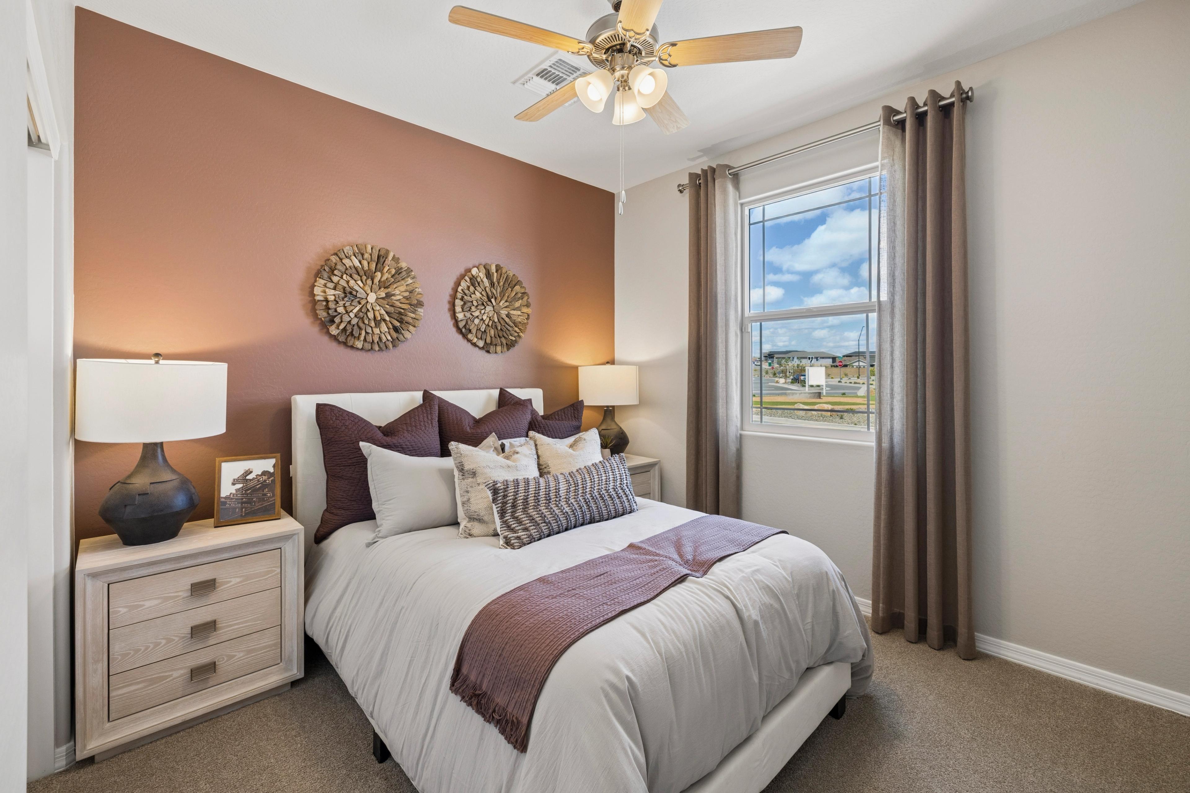 Cozy bedroom with queen bed, purple pillows, woven wall art, ceiling fan, and window view at Senator Cottages in Prescott AZ