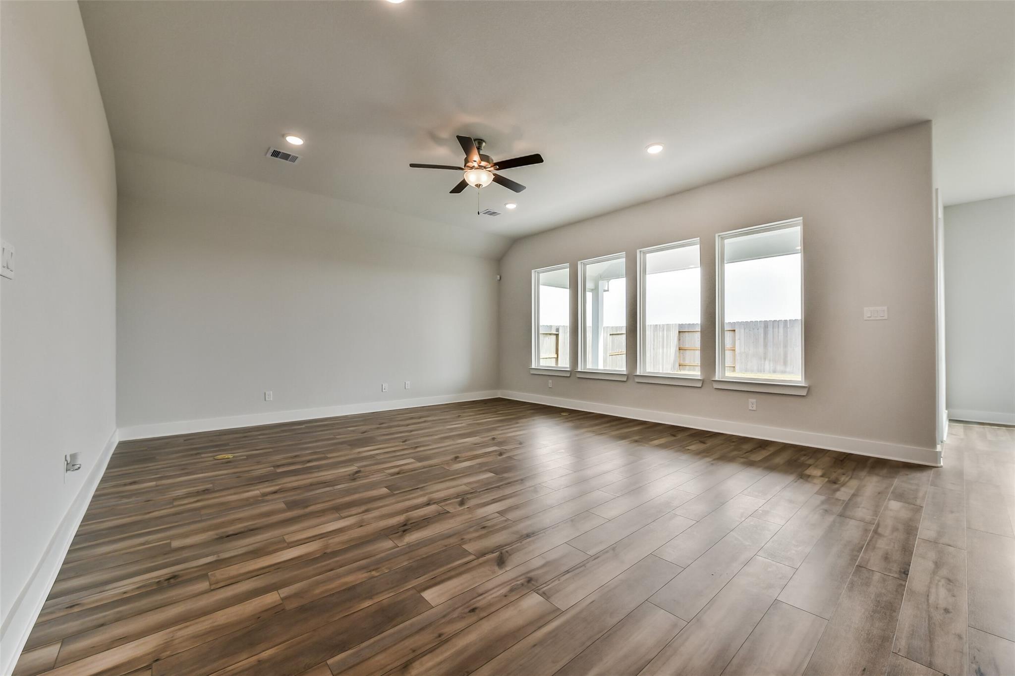 Spacious living room with hardwood floors, large triple windows, and ceiling fan in Davidson Homes The George A, Lago Mar, Texas City