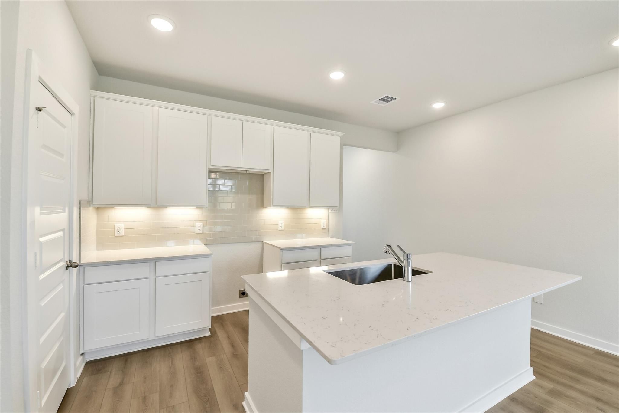 Bright modern kitchen with white shaker cabinets, quartz island sink, and recessed lighting in Davidson Homes Colorado F, Cleveland TX