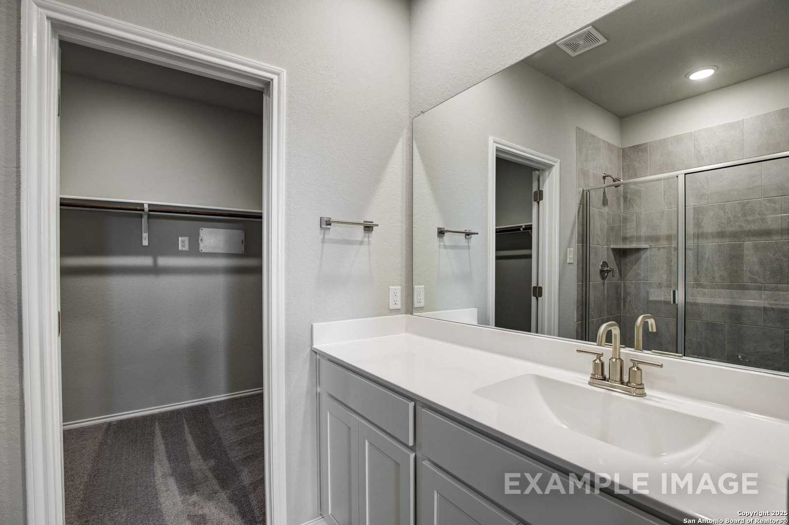 Modern master bathroom featuring double vanity, large frameless mirror, glass shower, and walk-in closet in Davidson Homes The Blanco C, San Antonio