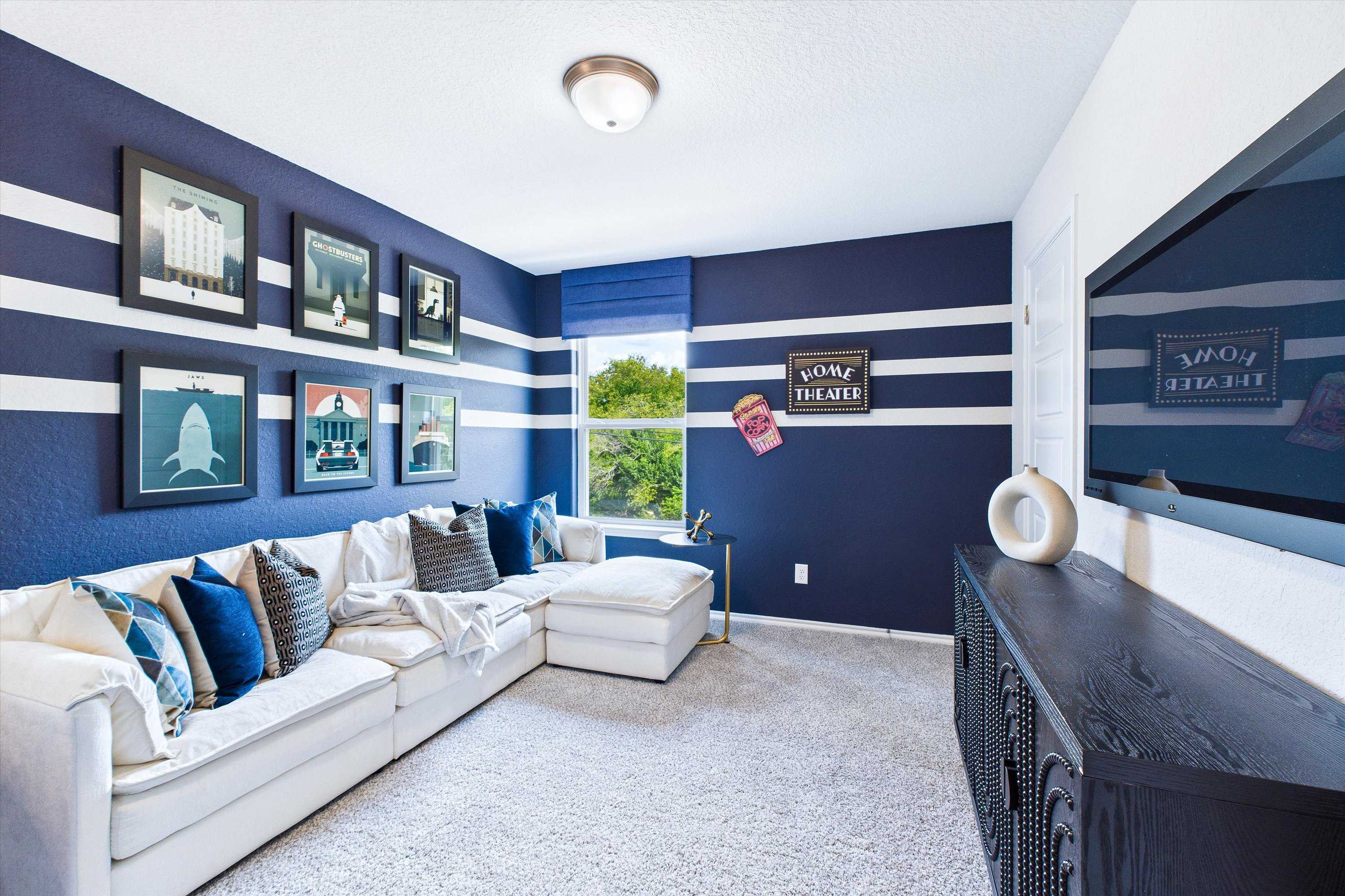 Navy blue striped game room at Cedar Heights in San Antonio TX with white L-shaped sectional, wall TV, and framed art