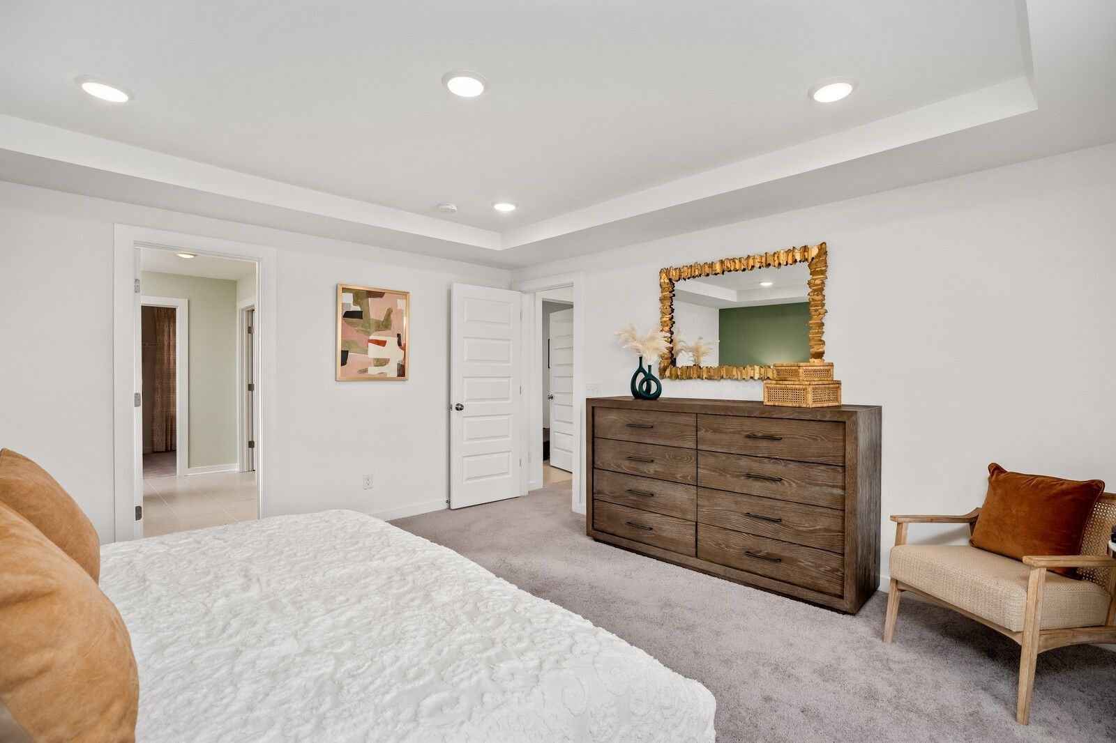 Elegant master bedroom with white tufted bed, wooden dresser, gold mirror, and recessed lighting in Davidson Homes The Gordon C, White House, TN