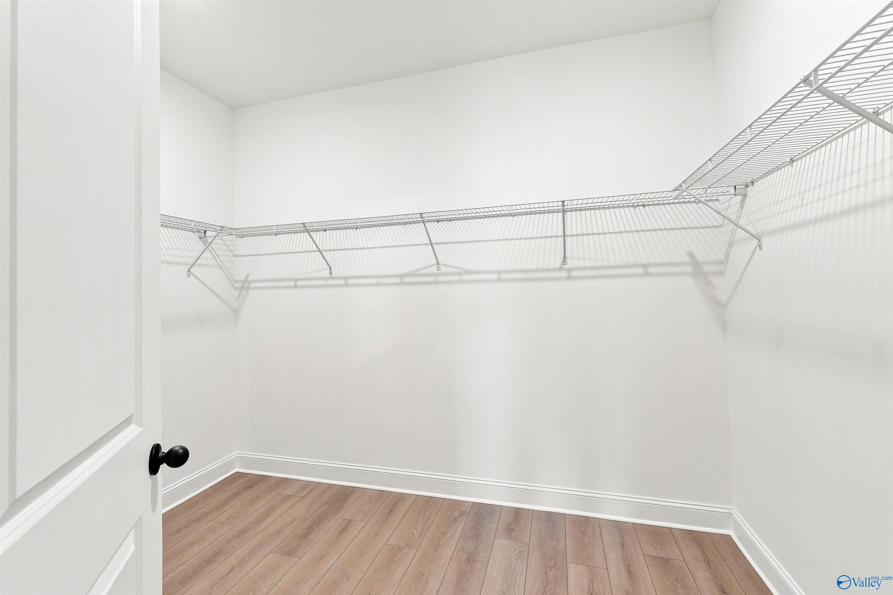 Walk-in closet with white wire shelving and wood-look flooring in The Oxford floor plan at Kendall Farms, Toney, Alabama.