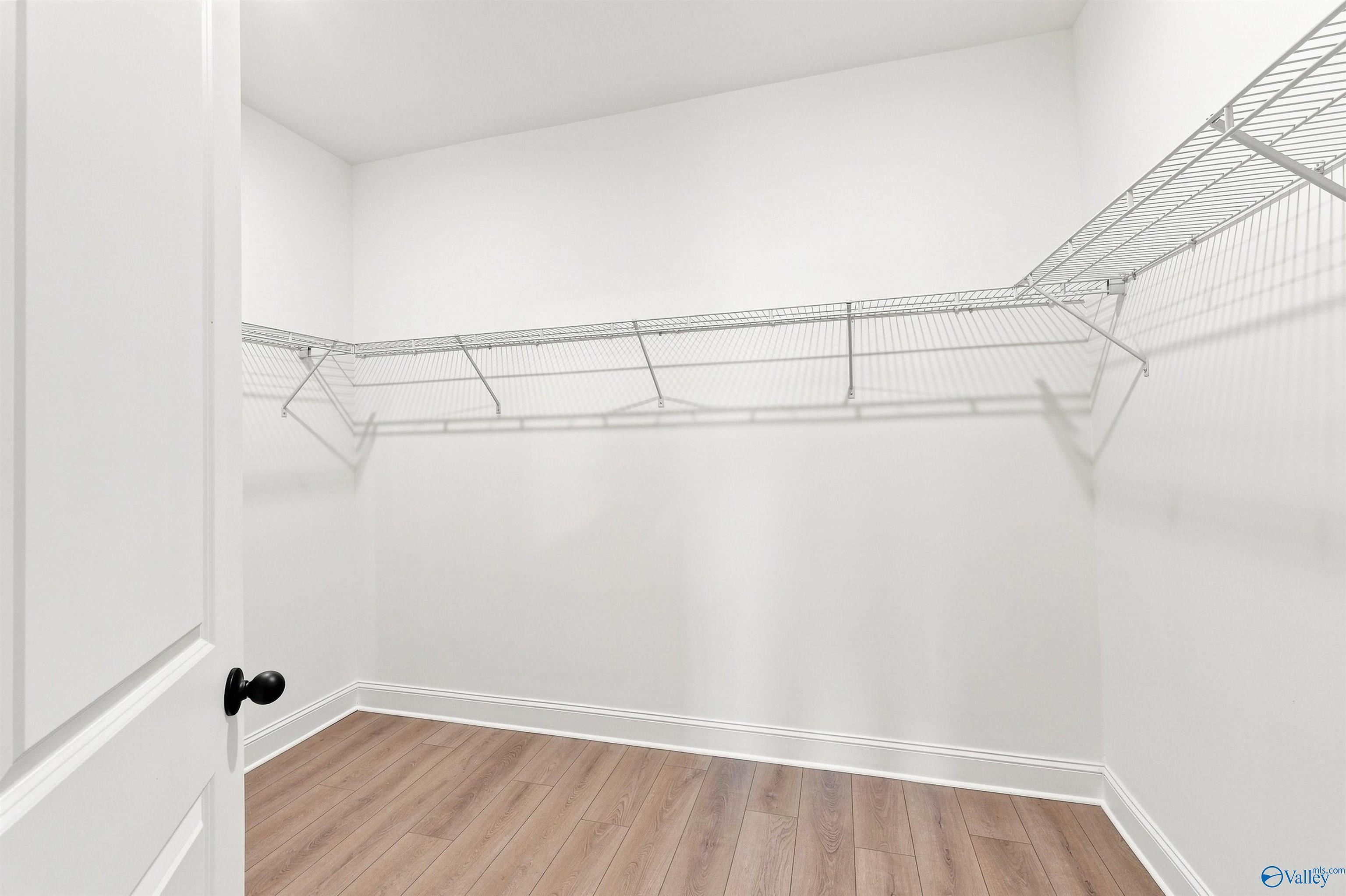 Walk-in closet with white wire shelving and wood-look flooring in The Oxford floor plan at Kendall Farms, Toney, Alabama.