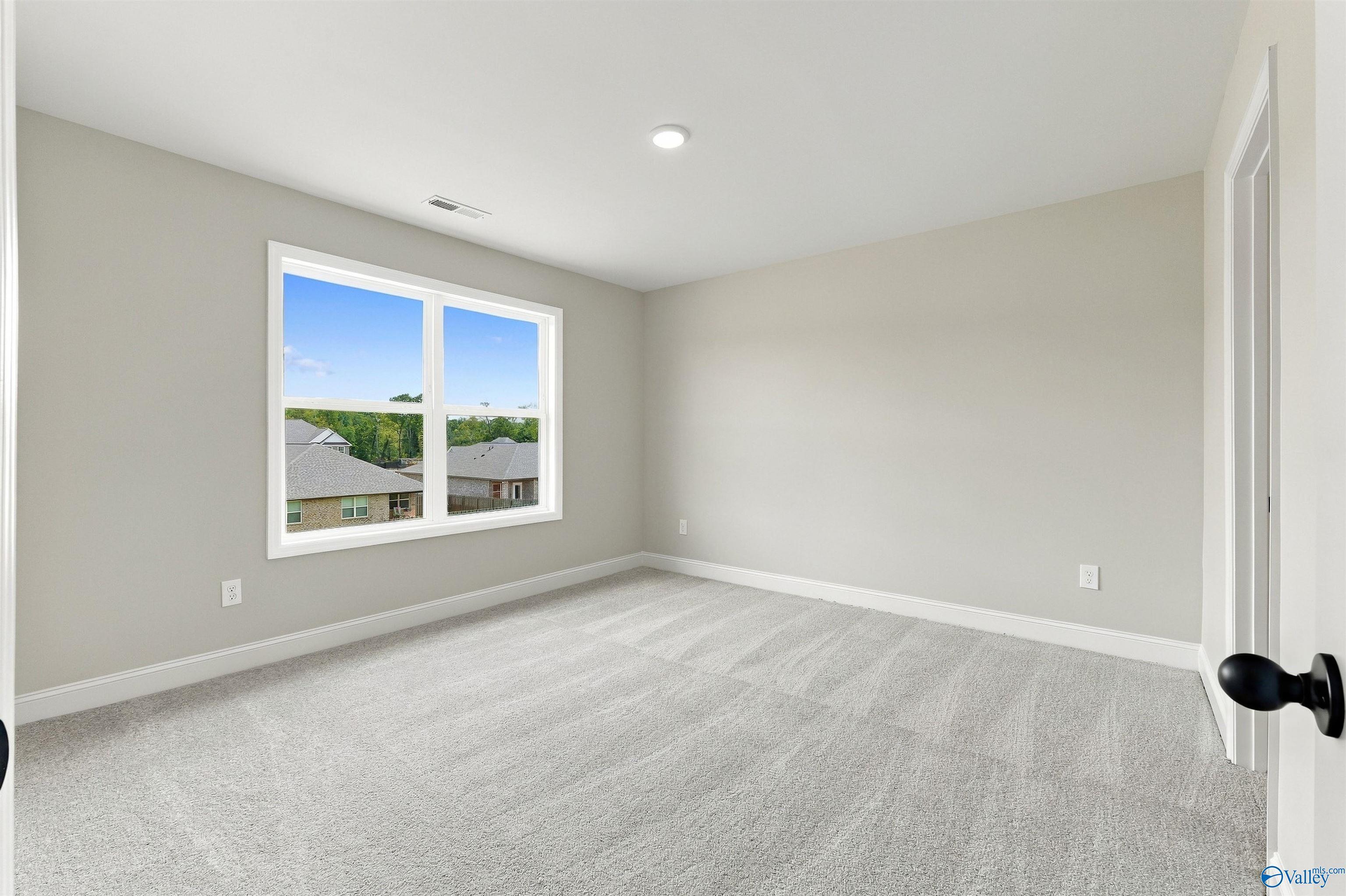Bright empty bedroom with carpet and large window overlooking neighborhood in Davidson Homes The Shelby A, Athens, Alabama