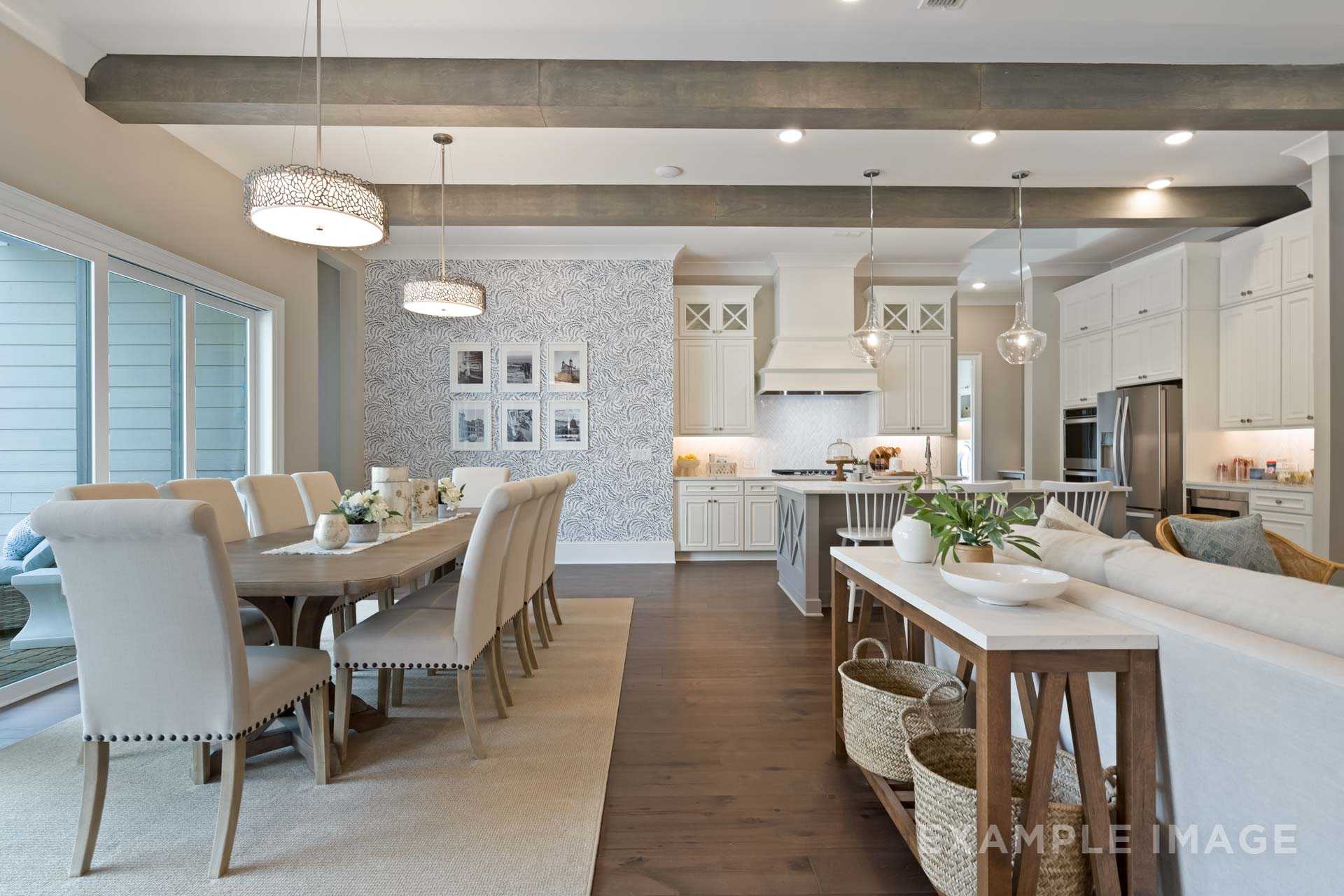 Open-concept kitchen, dining, and living area in The Seaside home design with wooden beams, white cabinets, and large island