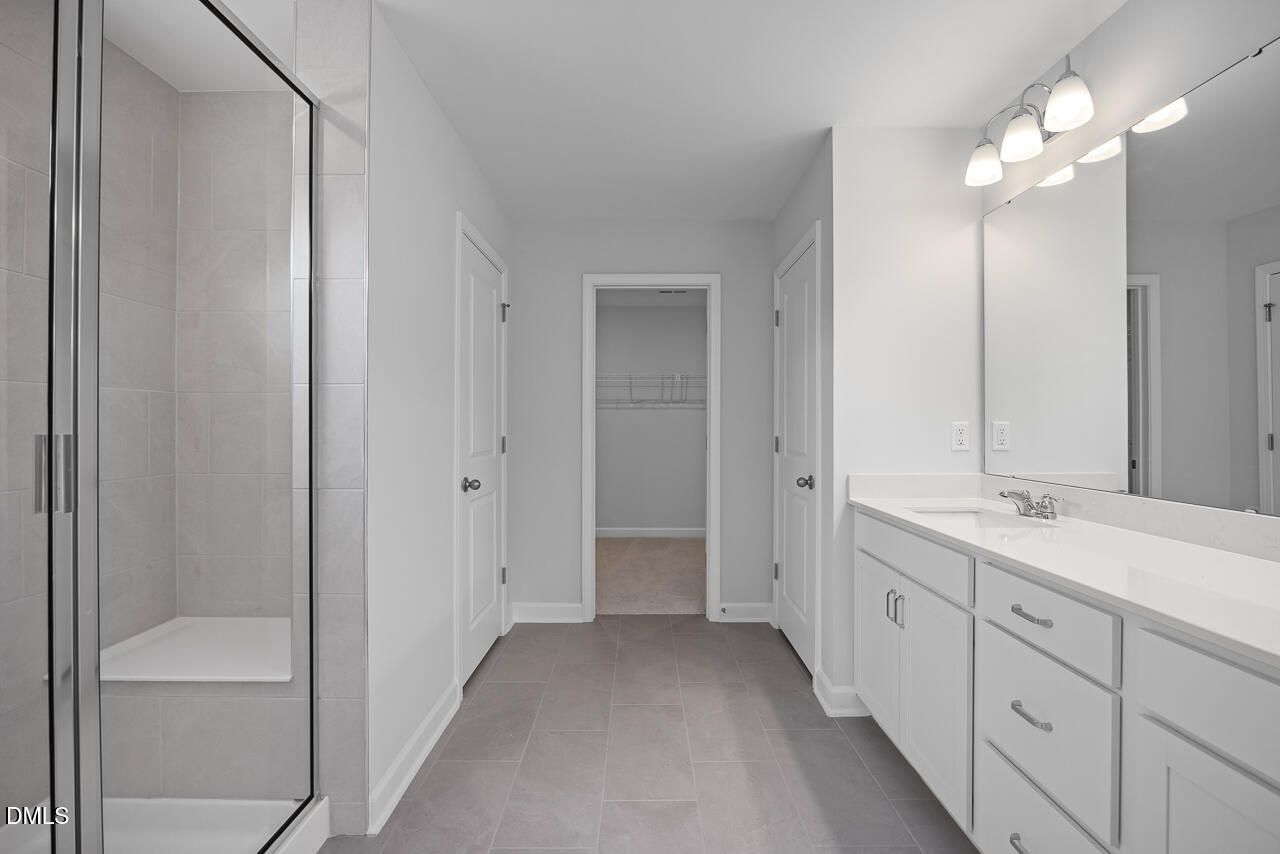 Modern master bathroom with frameless glass shower, quartz double vanity, and closet access in The Hickory II B, Zebulon, NC