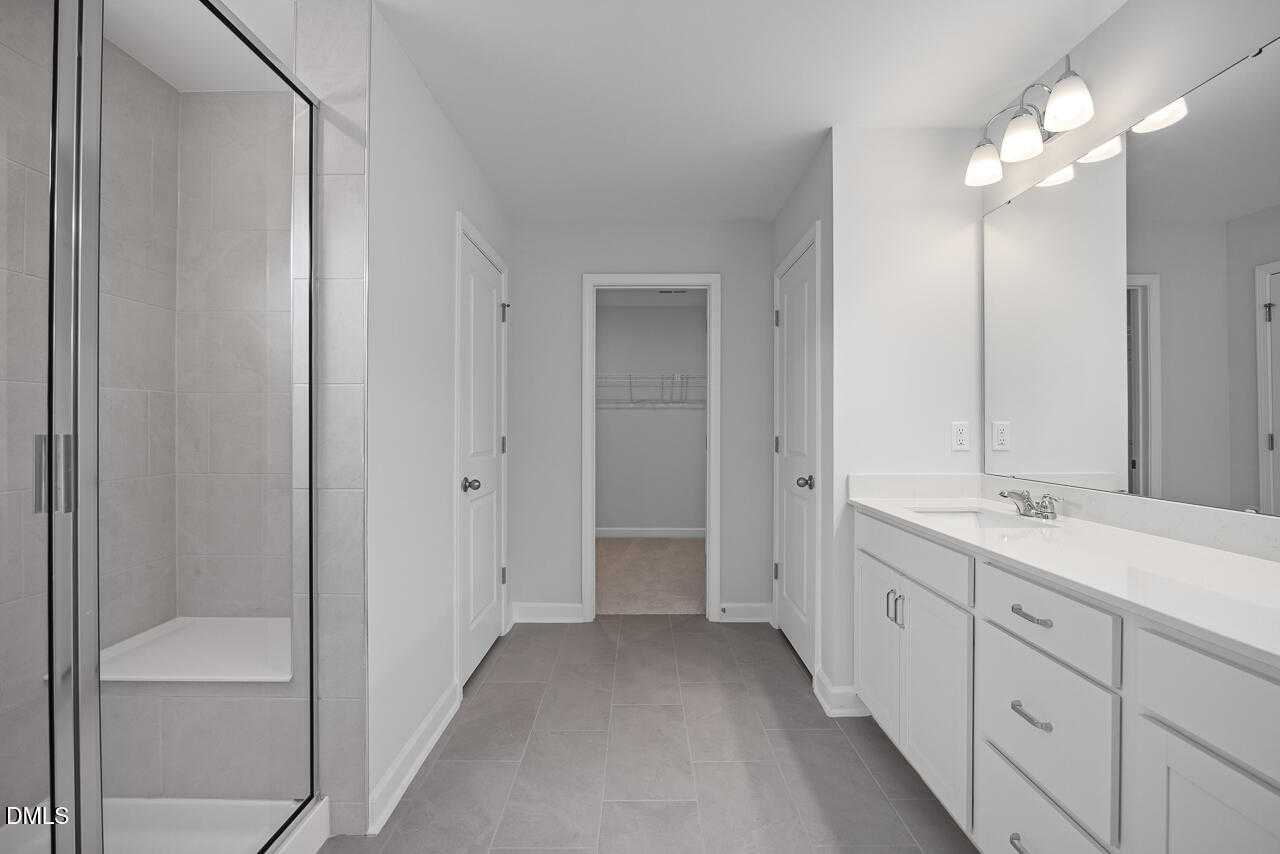 Modern master bathroom with frameless glass shower, quartz double vanity, and closet access in The Hickory II B, Zebulon, NC