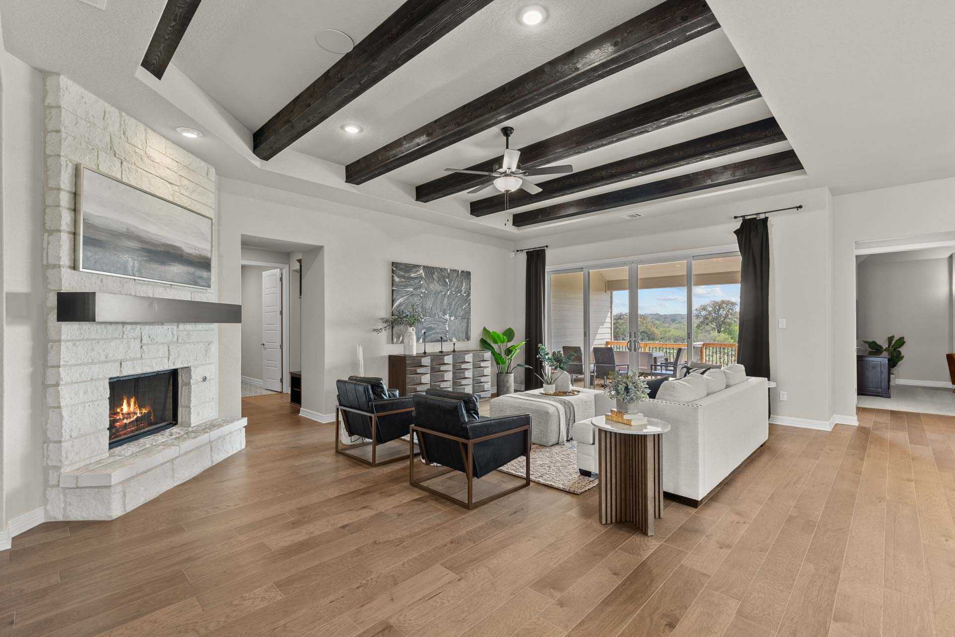 Spacious living room in The Summerlin B with exposed wood beam ceiling, white brick fireplace, modern seating, and patio views