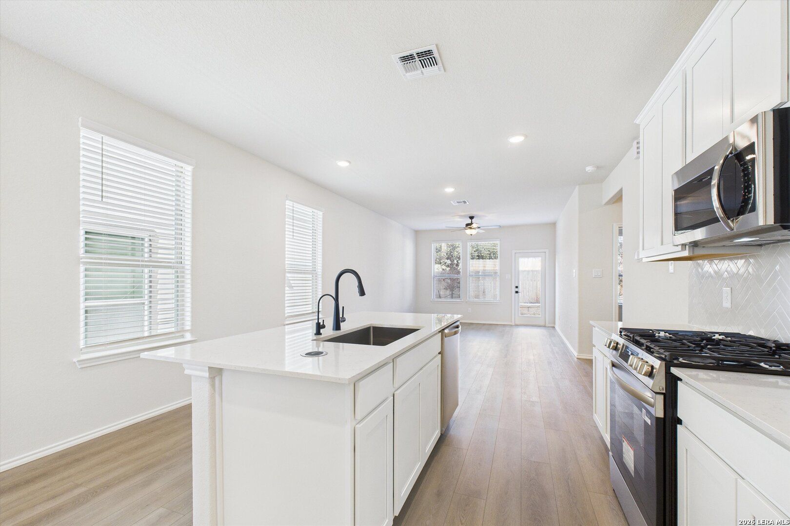 Modern white kitchen with island sink, stainless appliances, and open hardwood floors in Davidson Homes The Gillian B, San Antonio