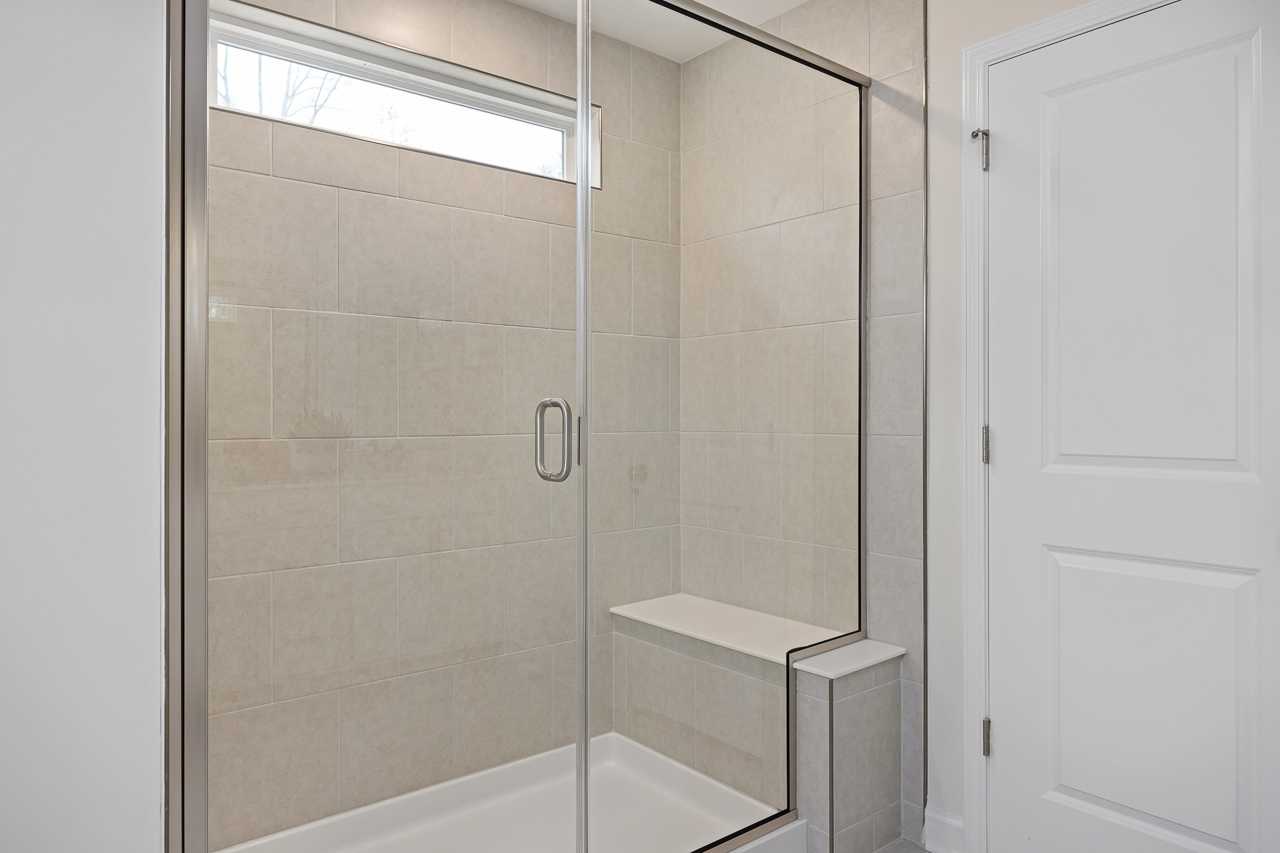 Spacious frameless glass shower at Gregory Village Townhomes in Lillington NC with beige tile walls and built-in bench