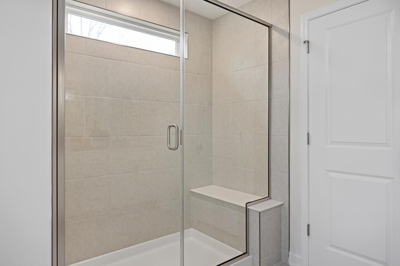 Spacious frameless glass shower at Gregory Village Townhomes in Lillington NC with beige tile walls and built-in bench