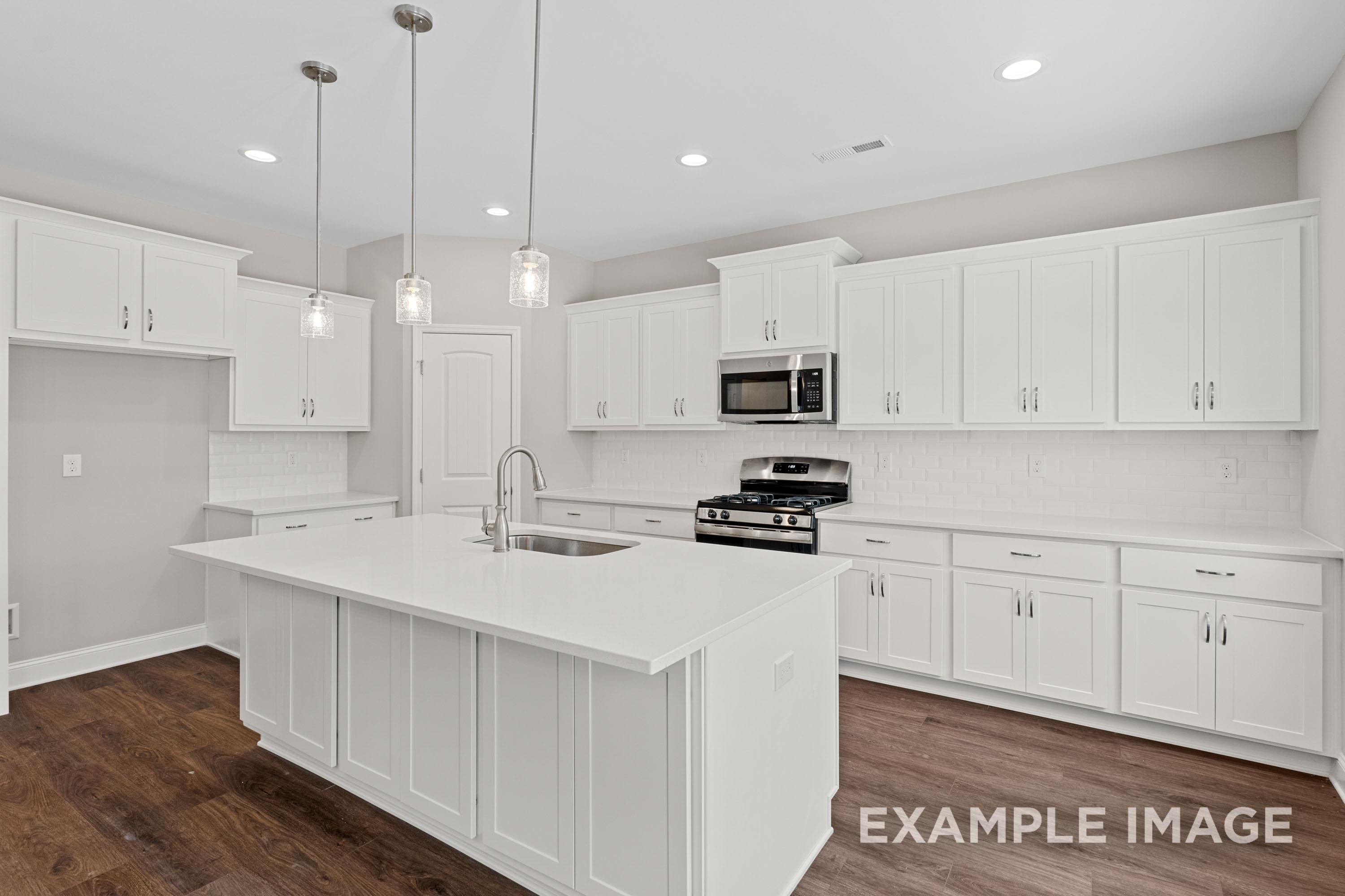 Spacious white kitchen in The Madison B with large island, gas range, subway tile backsplash, and pendant lights
