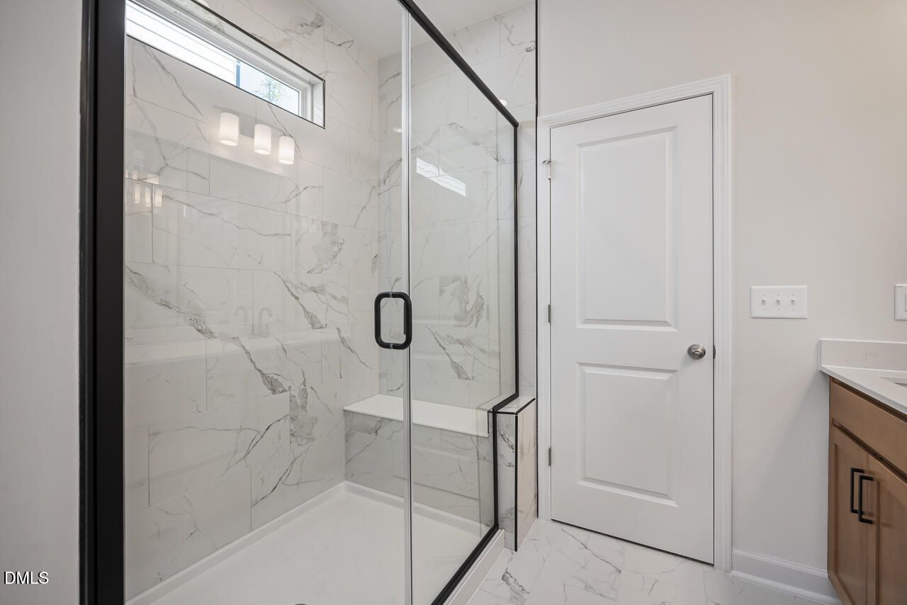 Modern primary bathroom walk-in shower with marble-look tile and glass door in The Ashport L at Sage on North Main.