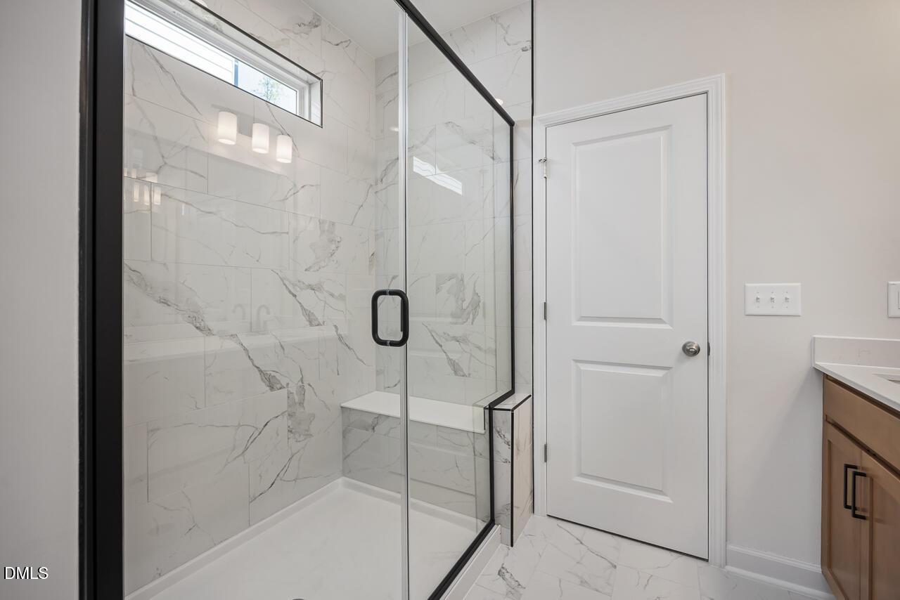 Modern primary bathroom walk-in shower with marble-look tile and glass door in The Ashport L at Sage on North Main.