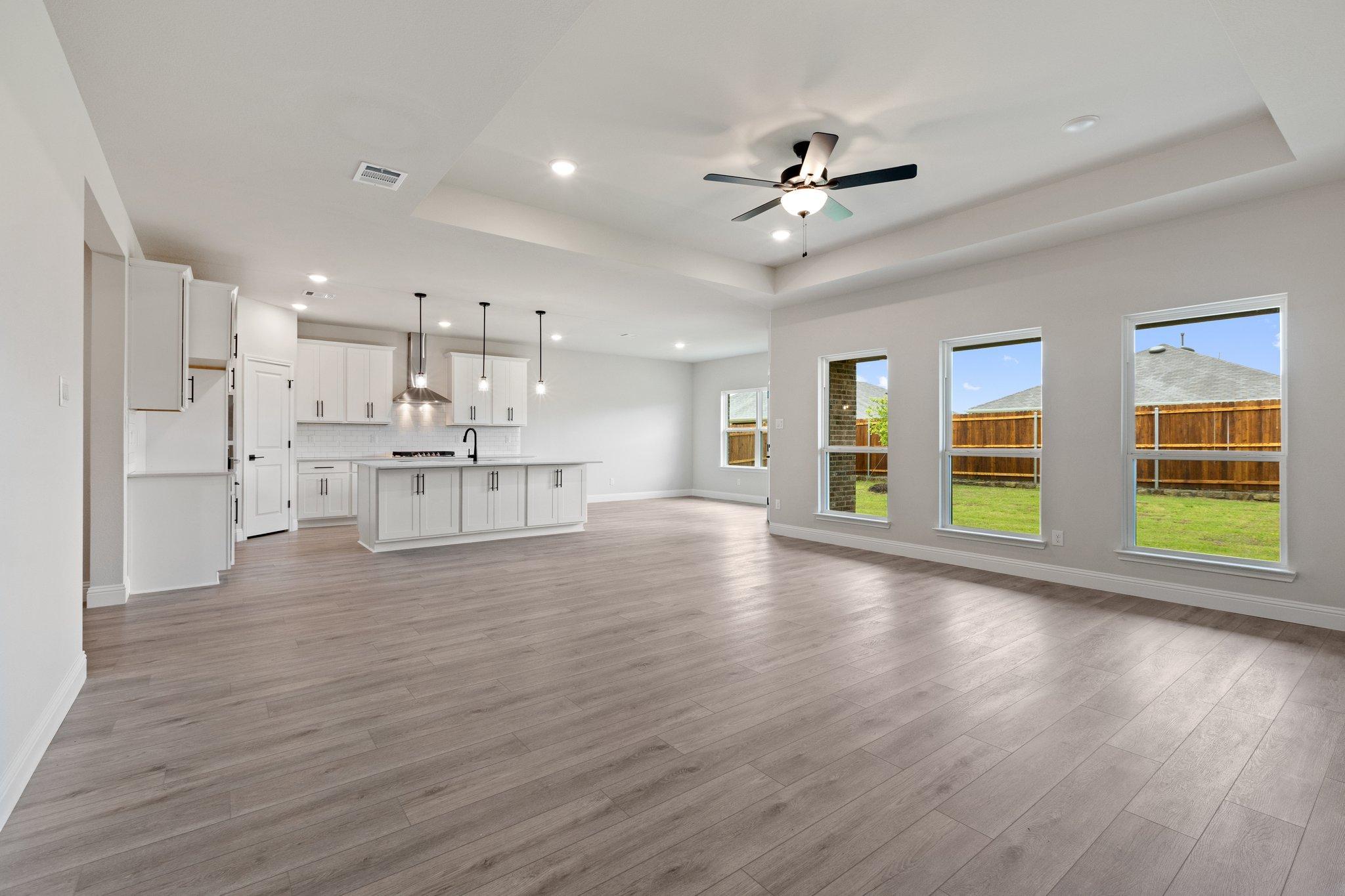 Spacious open-concept kitchen in The Harrison with white cabinets, large island, hardwood floors, and large windows to backyard