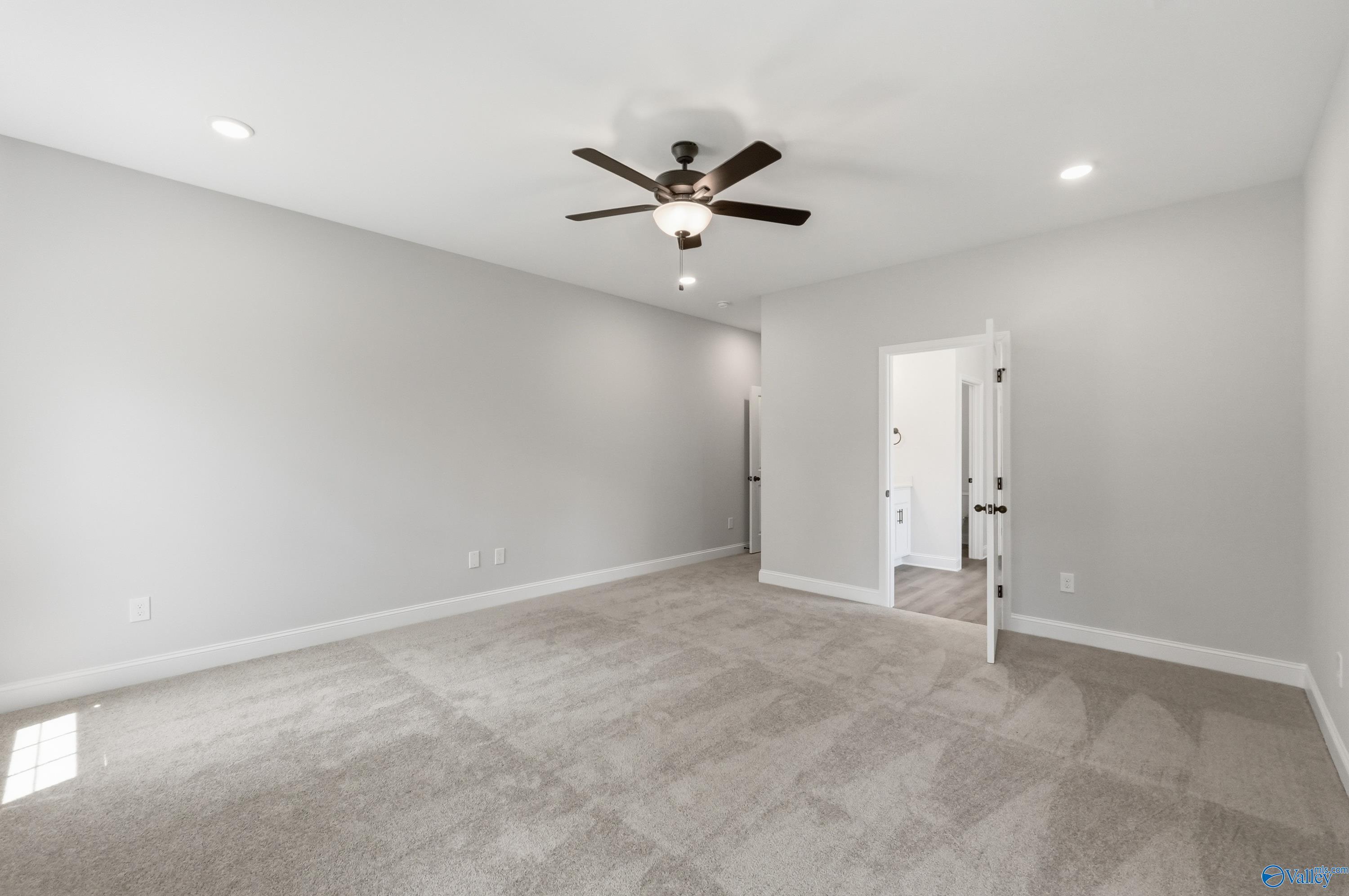 Spacious bedroom with gray walls, beige carpet, ceiling fan, and open en-suite bathroom door in Davidson Homes The Rockford B, Athens AL